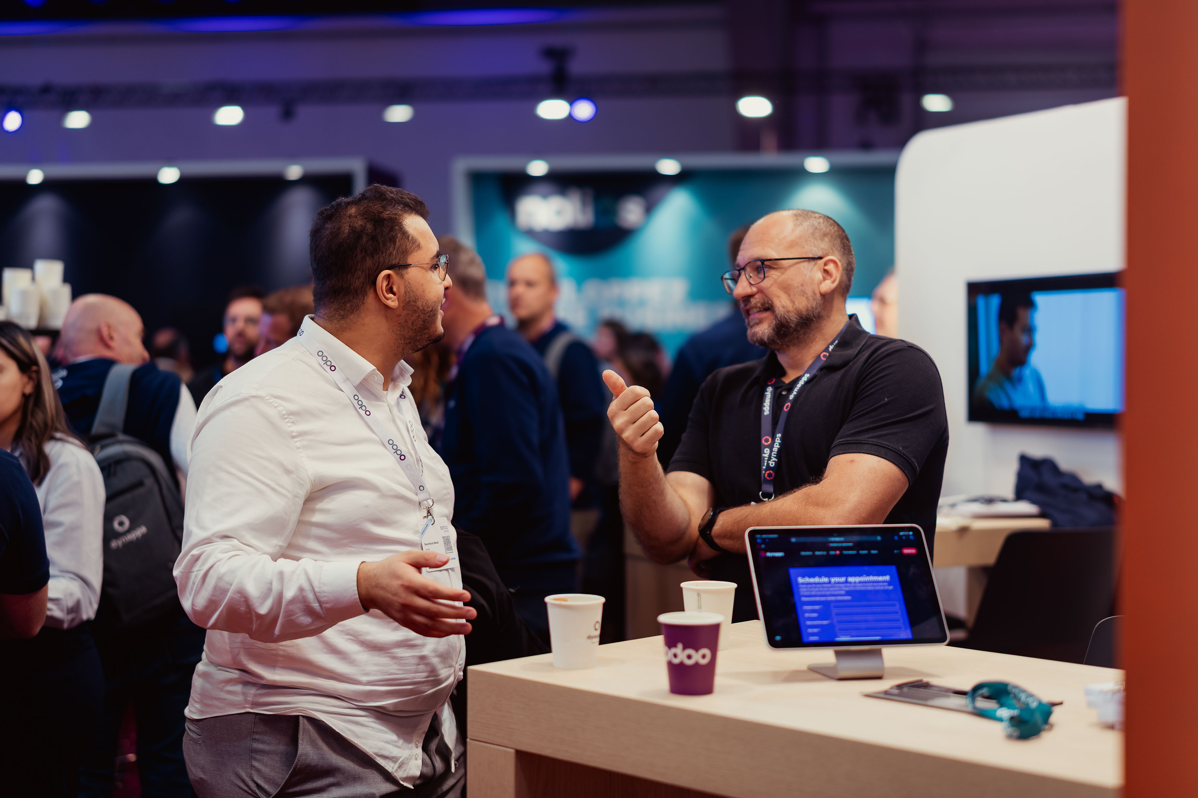 Two attendees chatting over coffee near a demo tablet