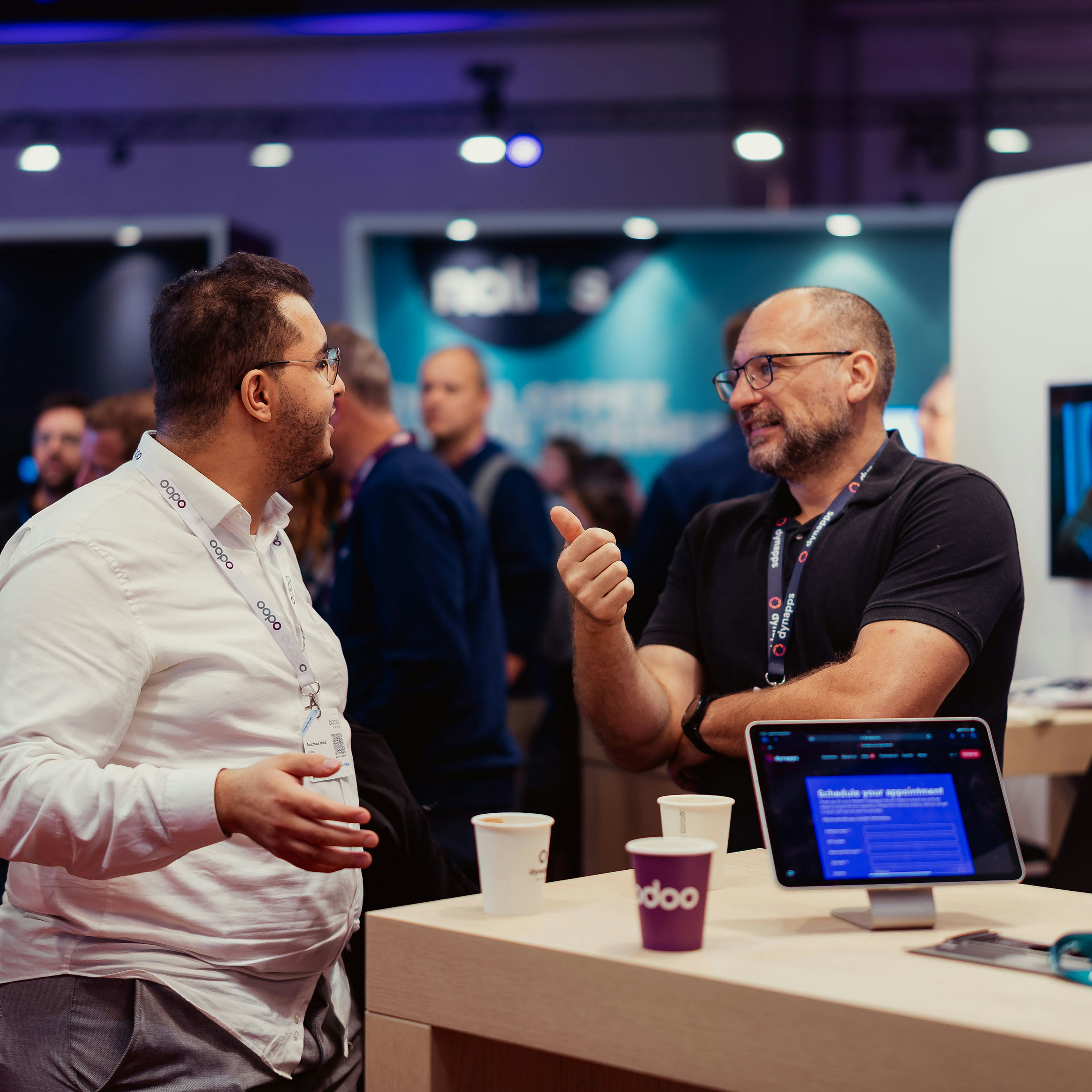 Two attendees chatting over coffee near a demo tablet