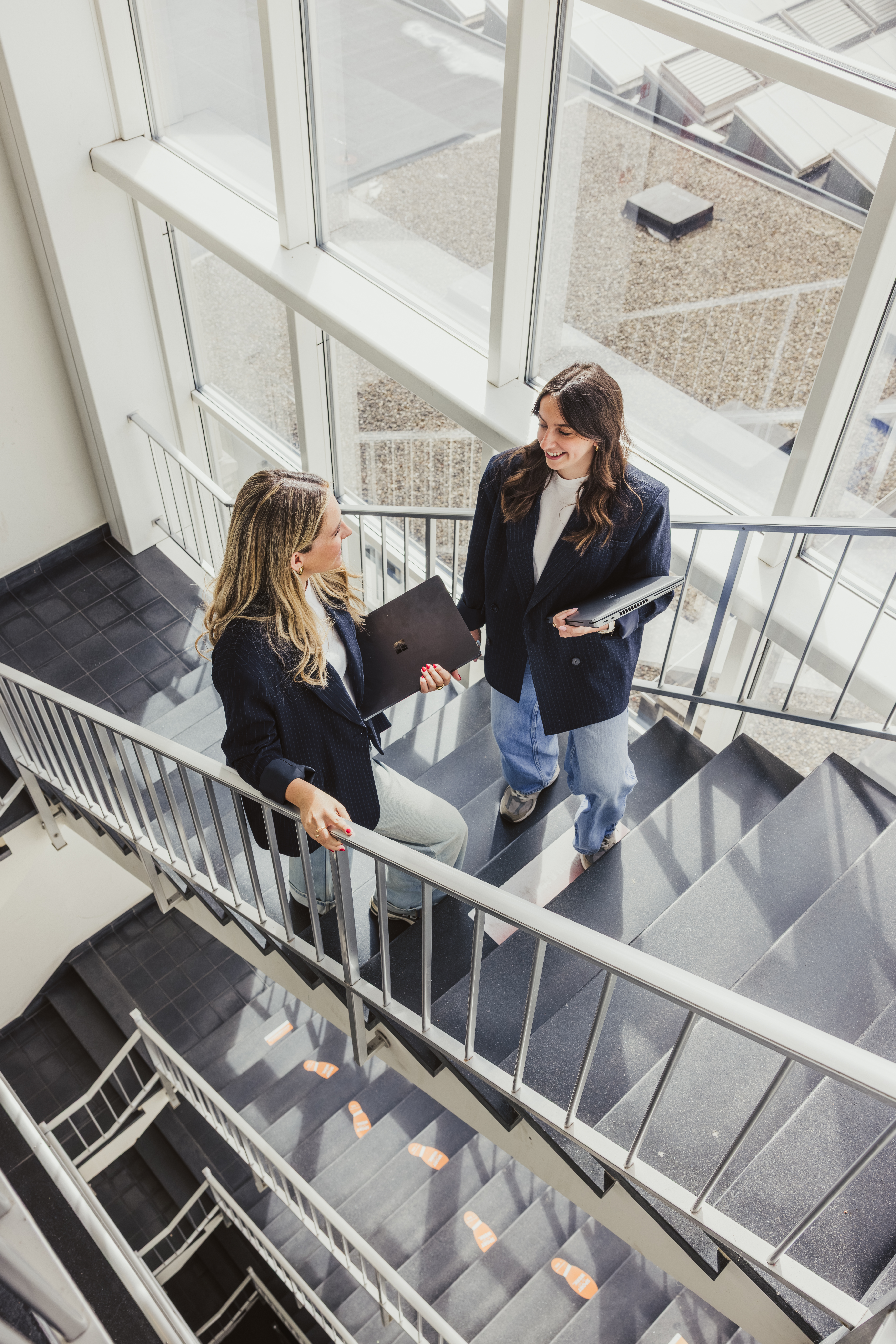 Two colleagues talking with laptops in a bright stairwell