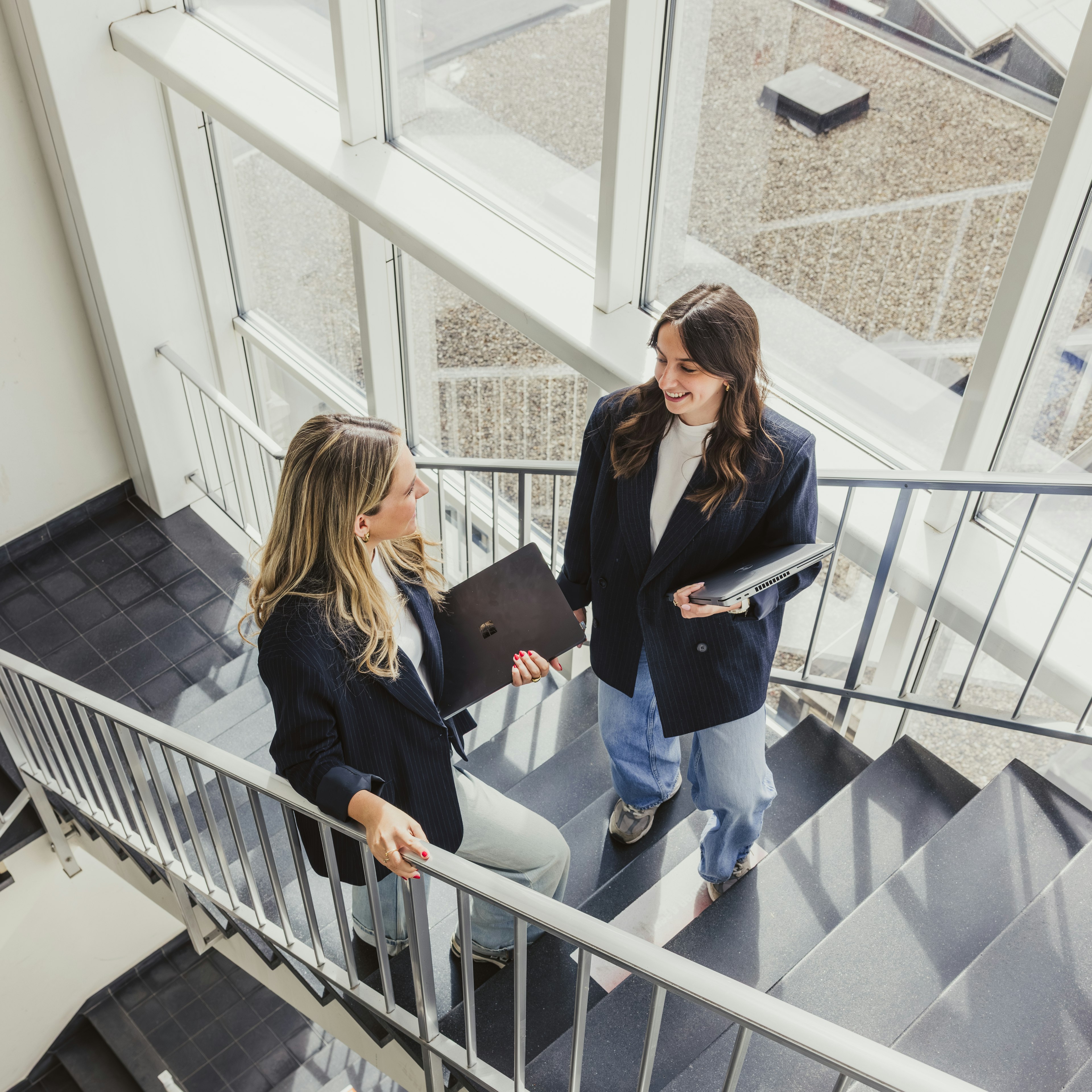 Deux collègues discutent devant leurs ordinateurs portables dans une cage d'escalier bien éclairée