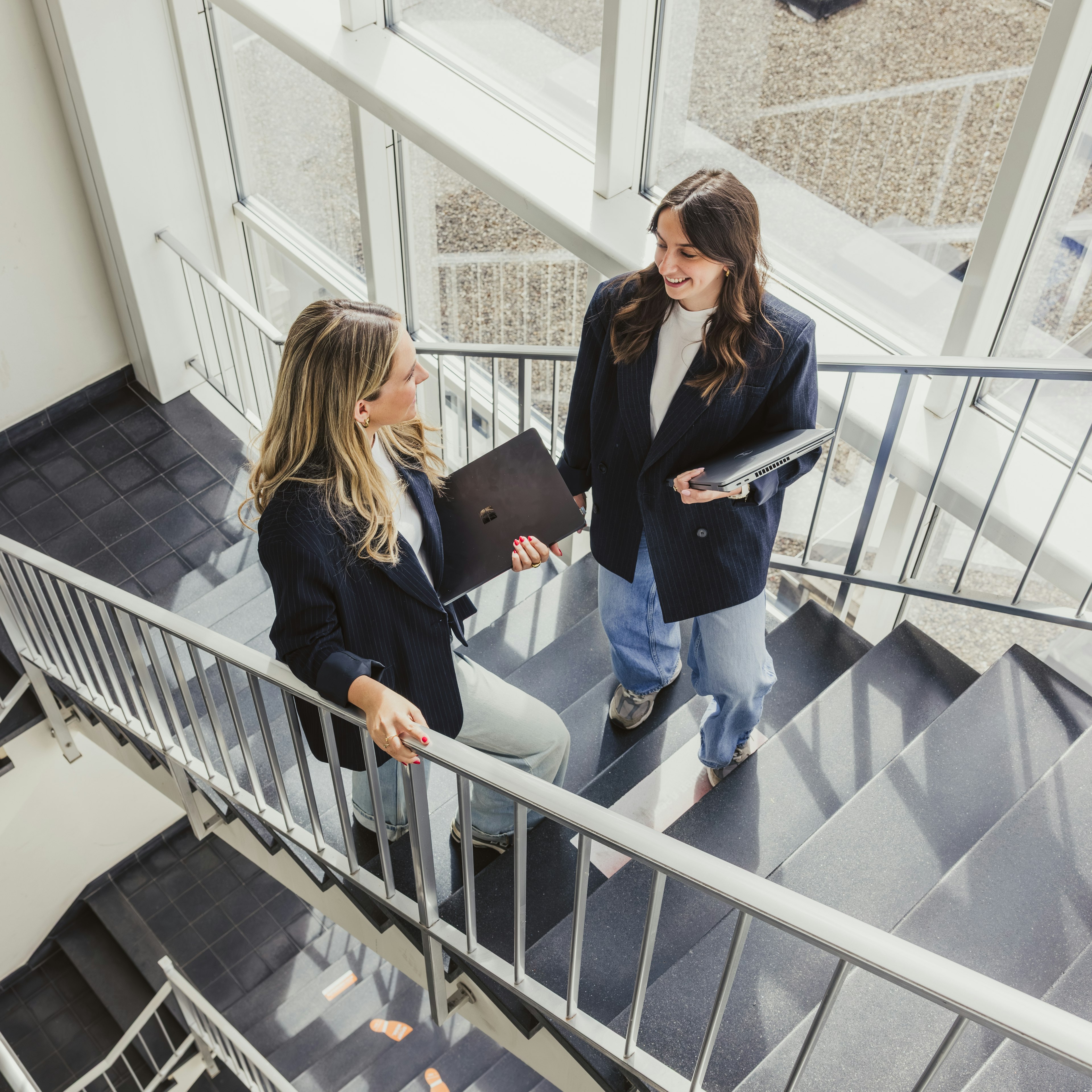 Two colleagues talking with laptops in a bright stairwell