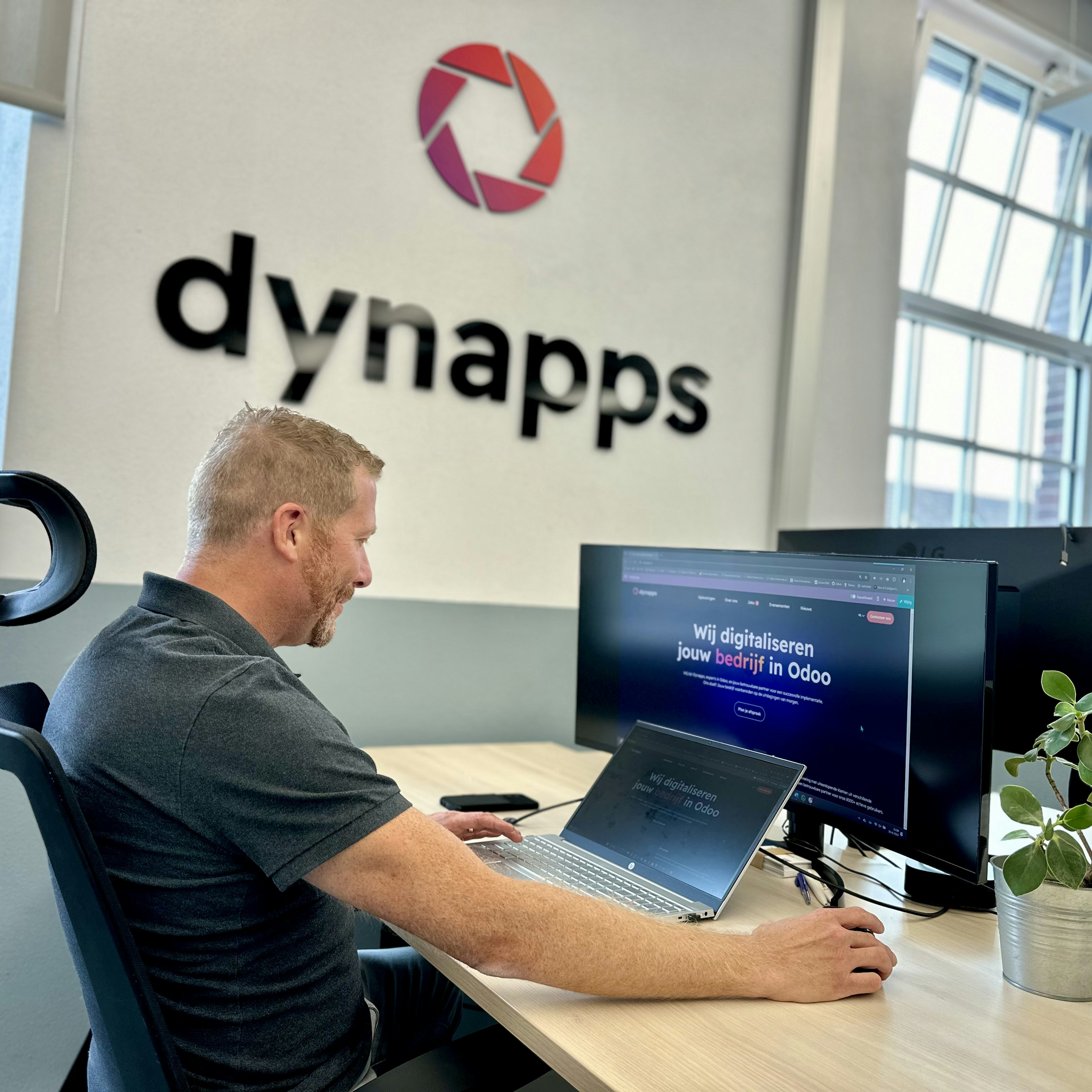 Man working at a desk under the Dynapps office logo
