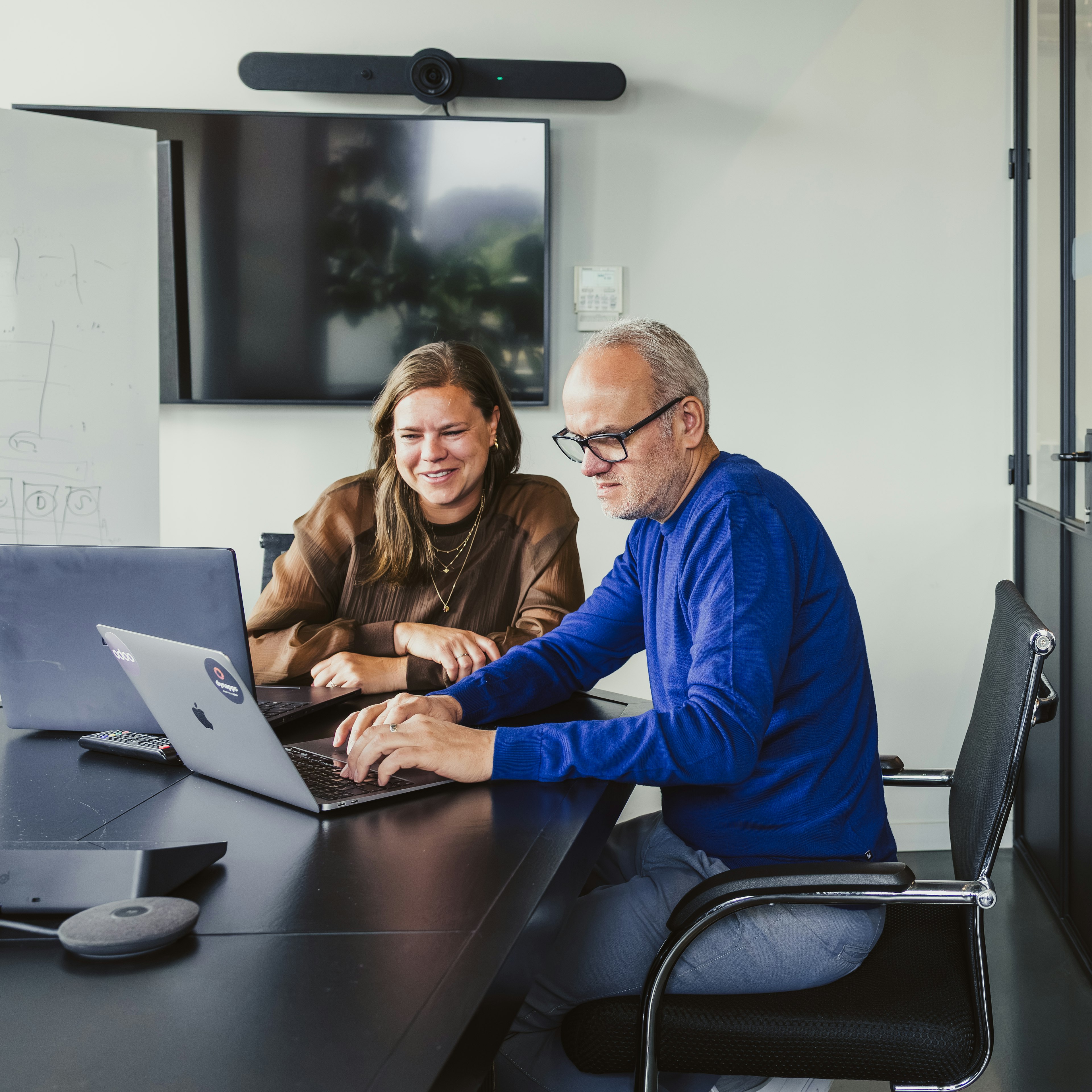Two colleagues collaborating on a laptop in a meeting room