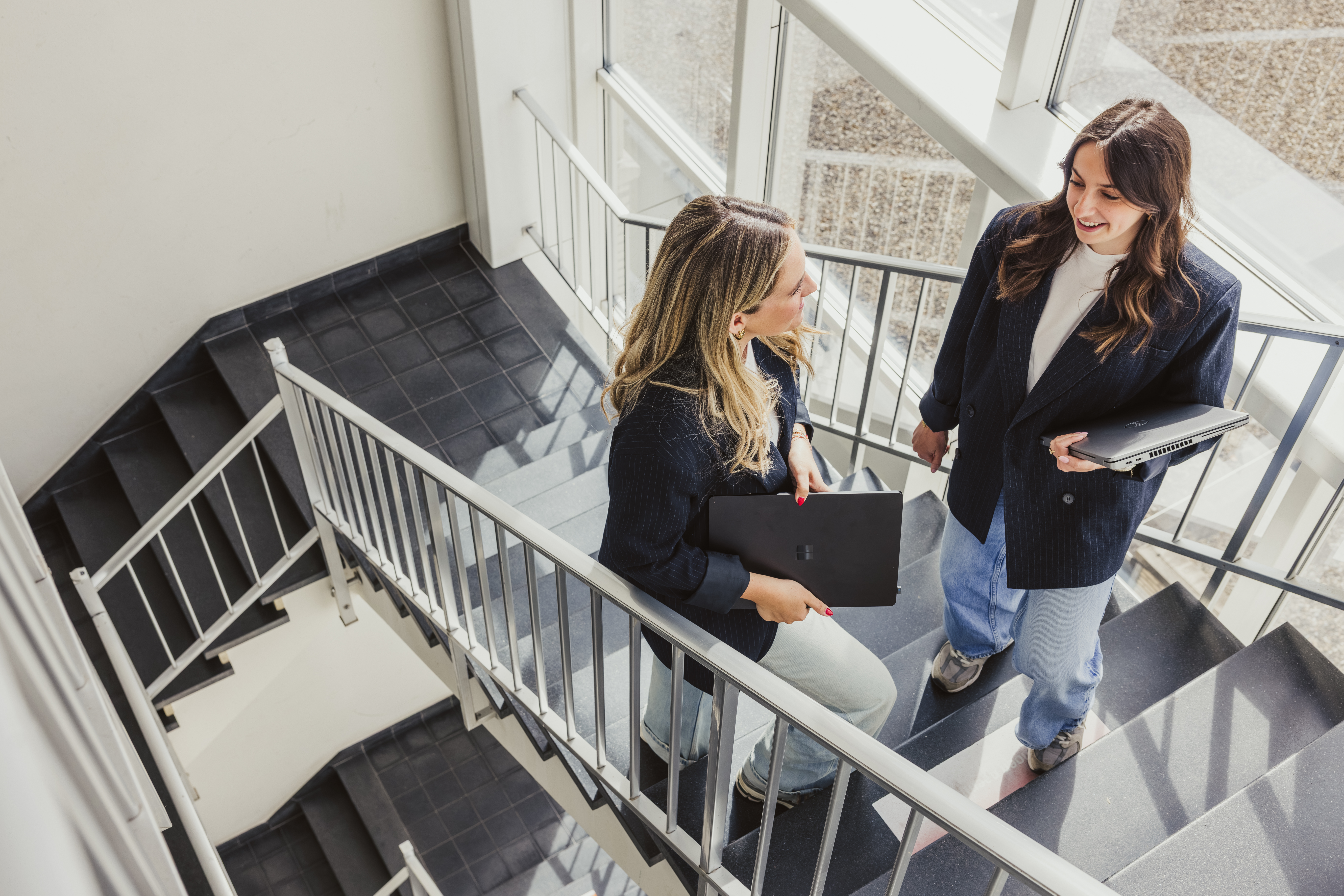 Two women with laptops chatting on the office stairs