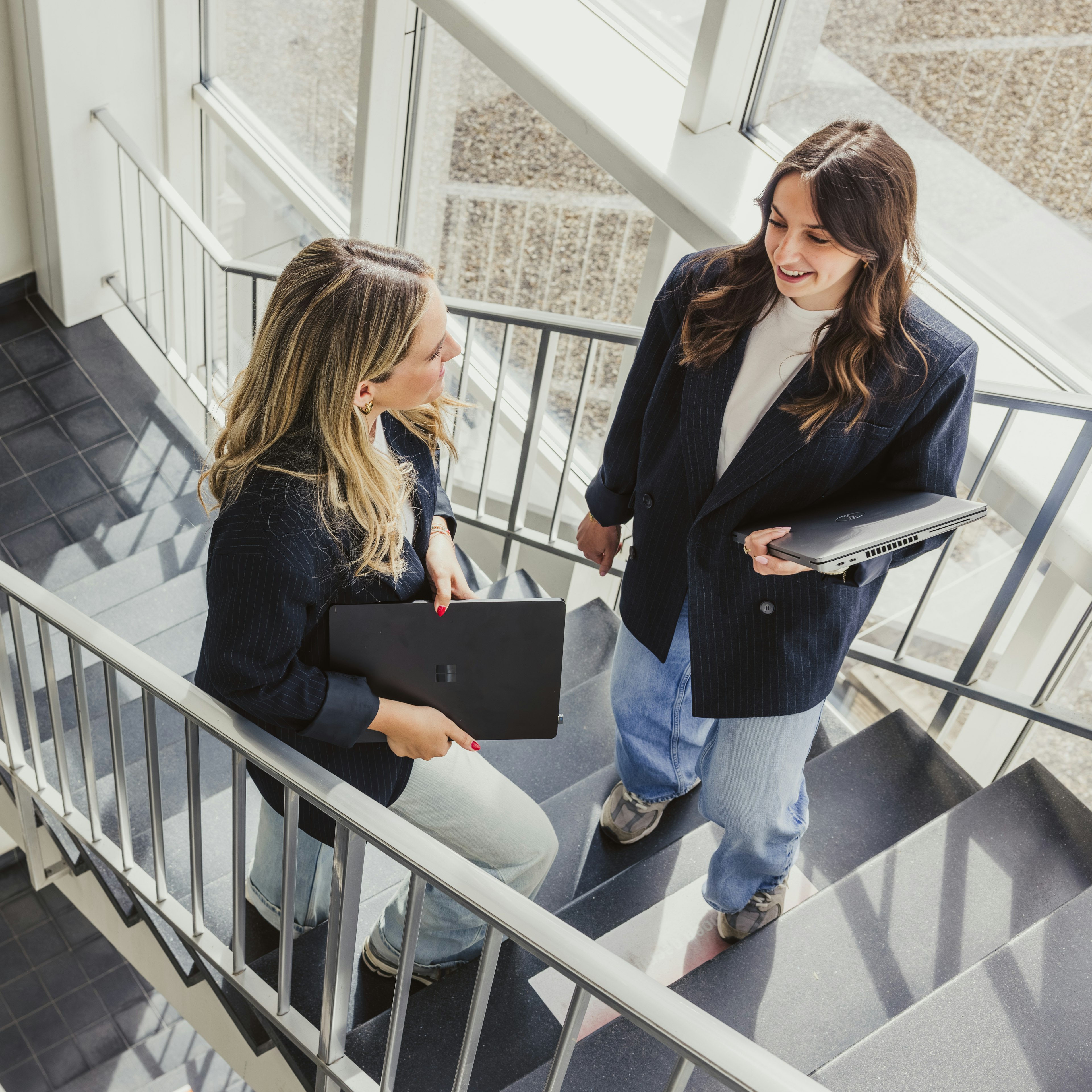 Two women with laptops chatting on the office stairs