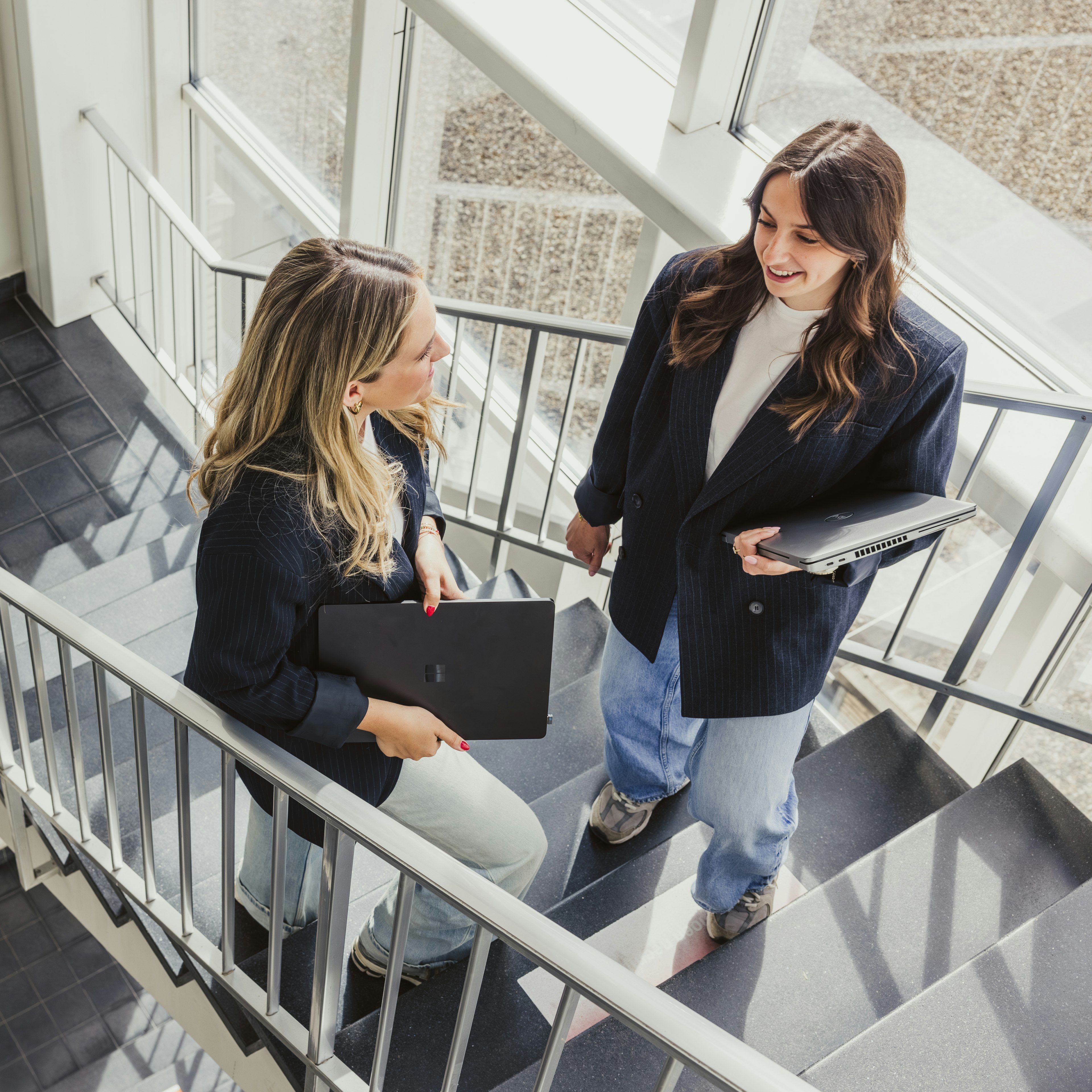 Two women with laptops chatting on the office stairs