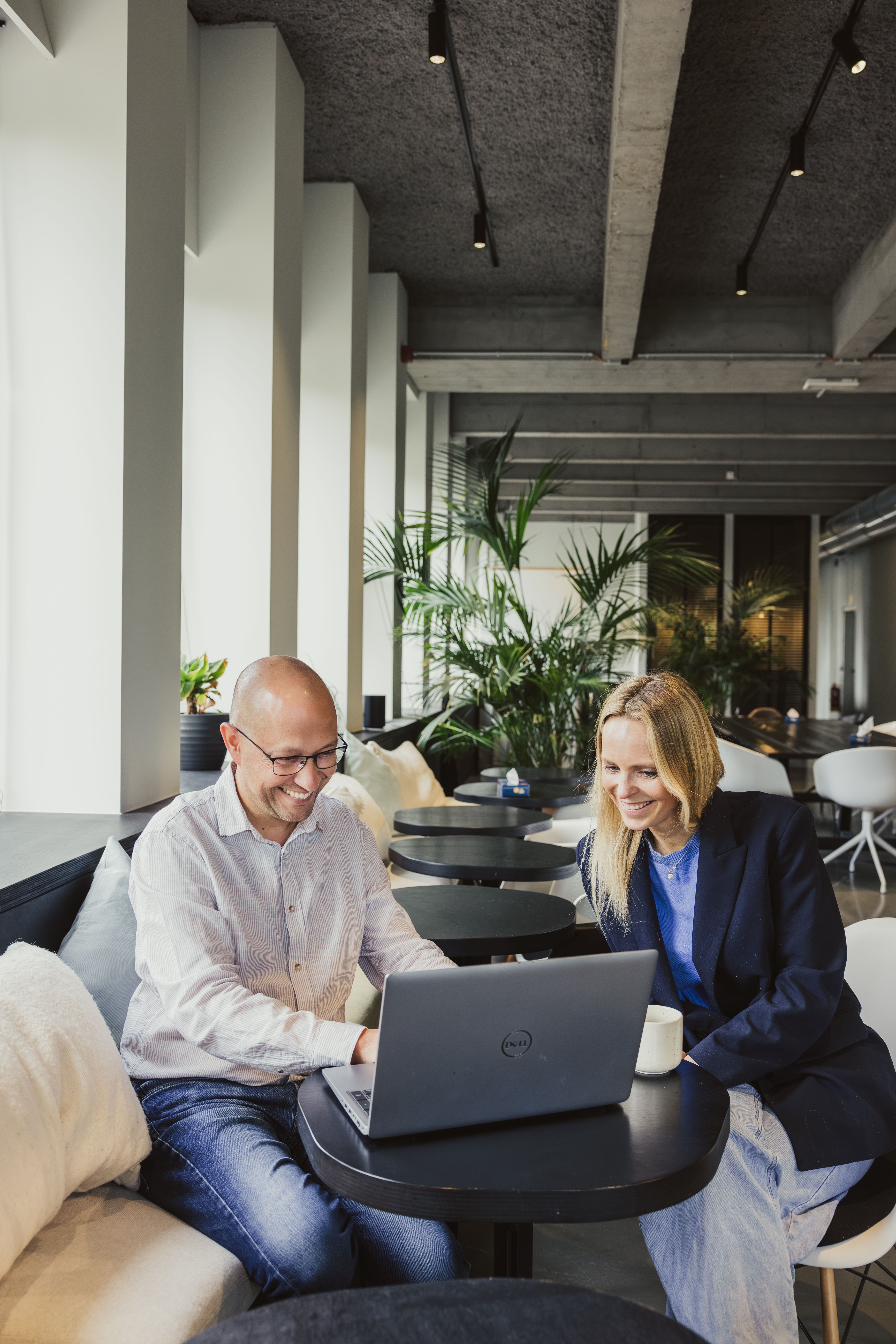 Collega’s die glimlachen terwijl ze achter een laptop zitten in een werkruimte in caféstijl