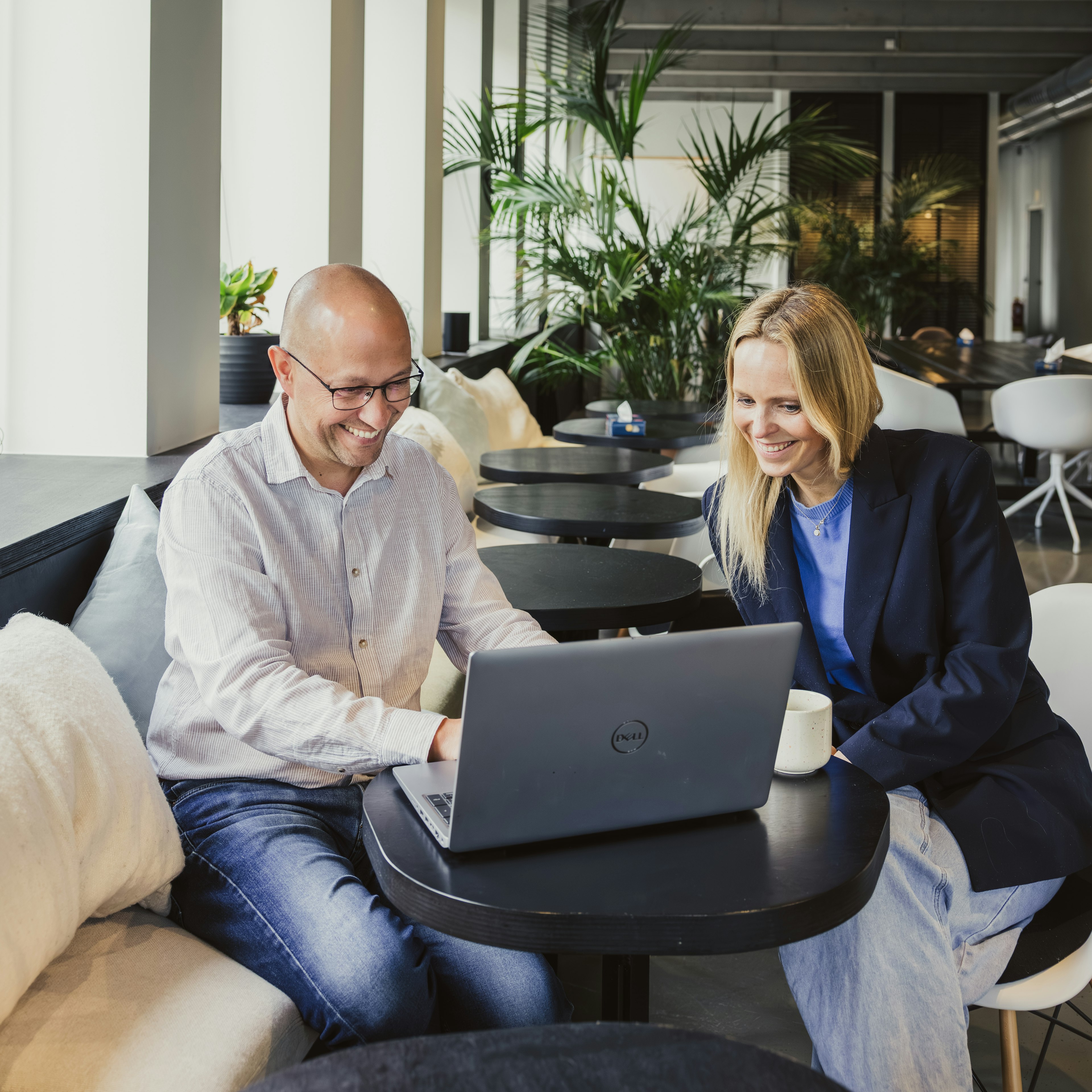 Collega’s die glimlachen terwijl ze achter een laptop zitten in een werkruimte in caféstijl