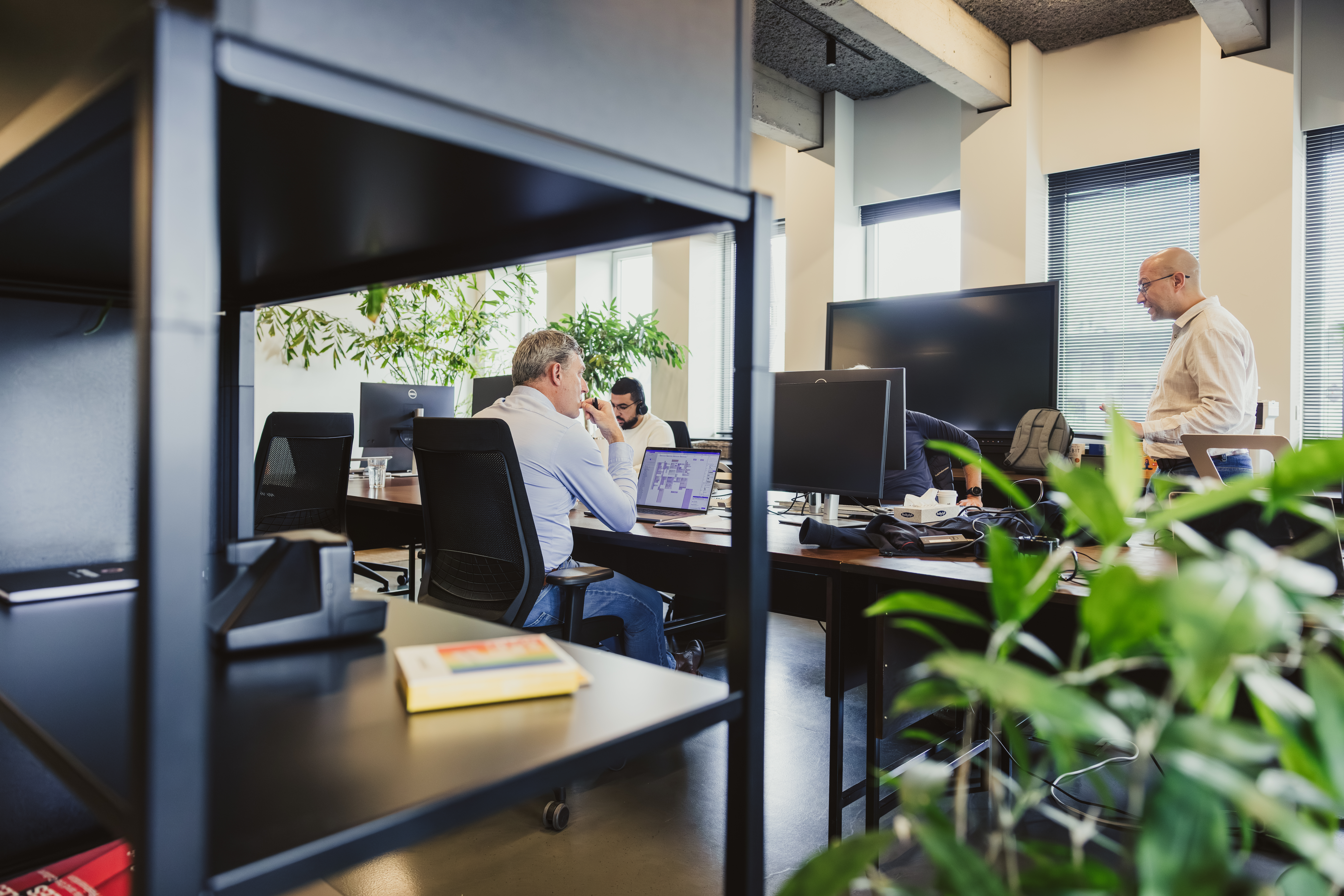Developers at desks seen through an office bookshelf
