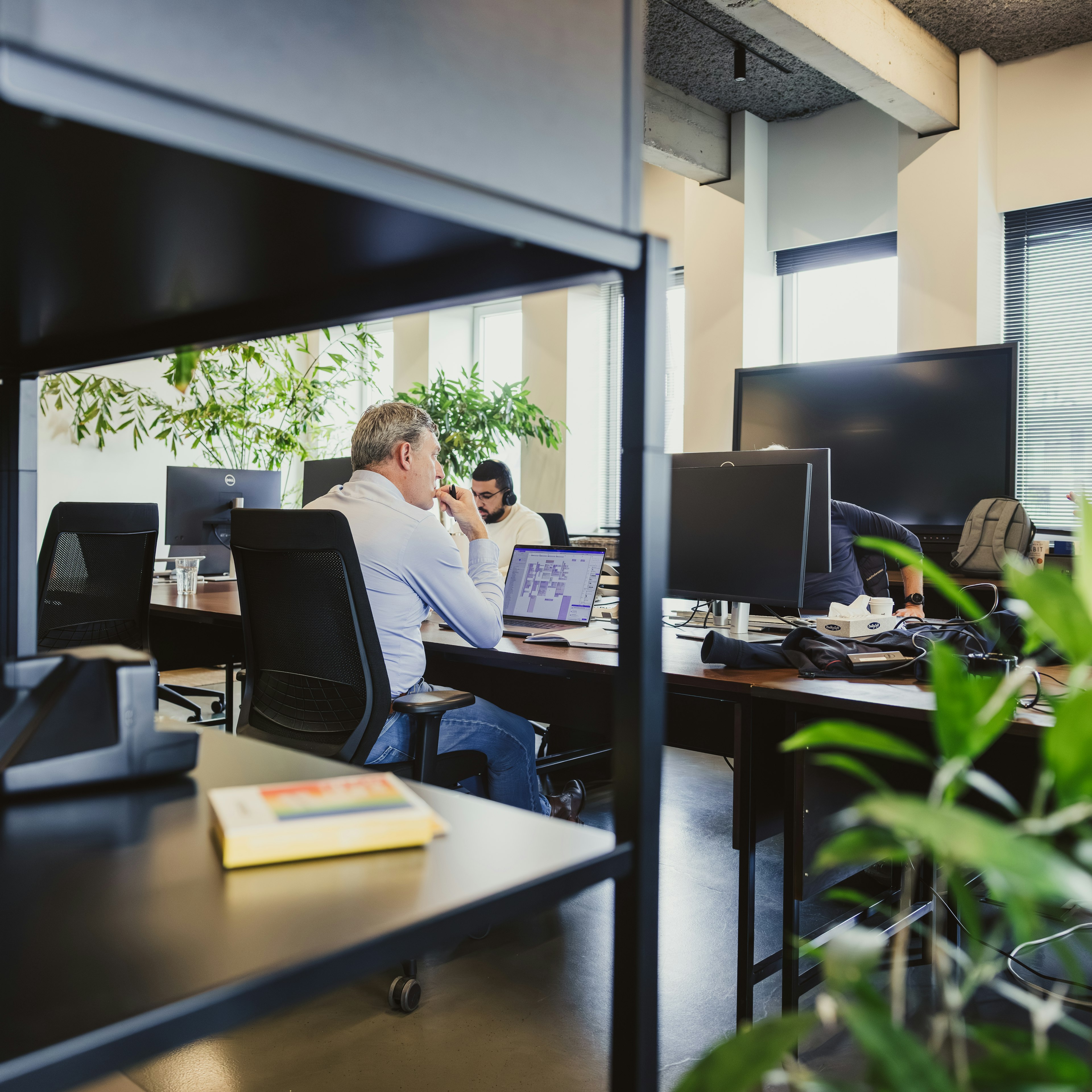 Developers at desks seen through an office bookshelf