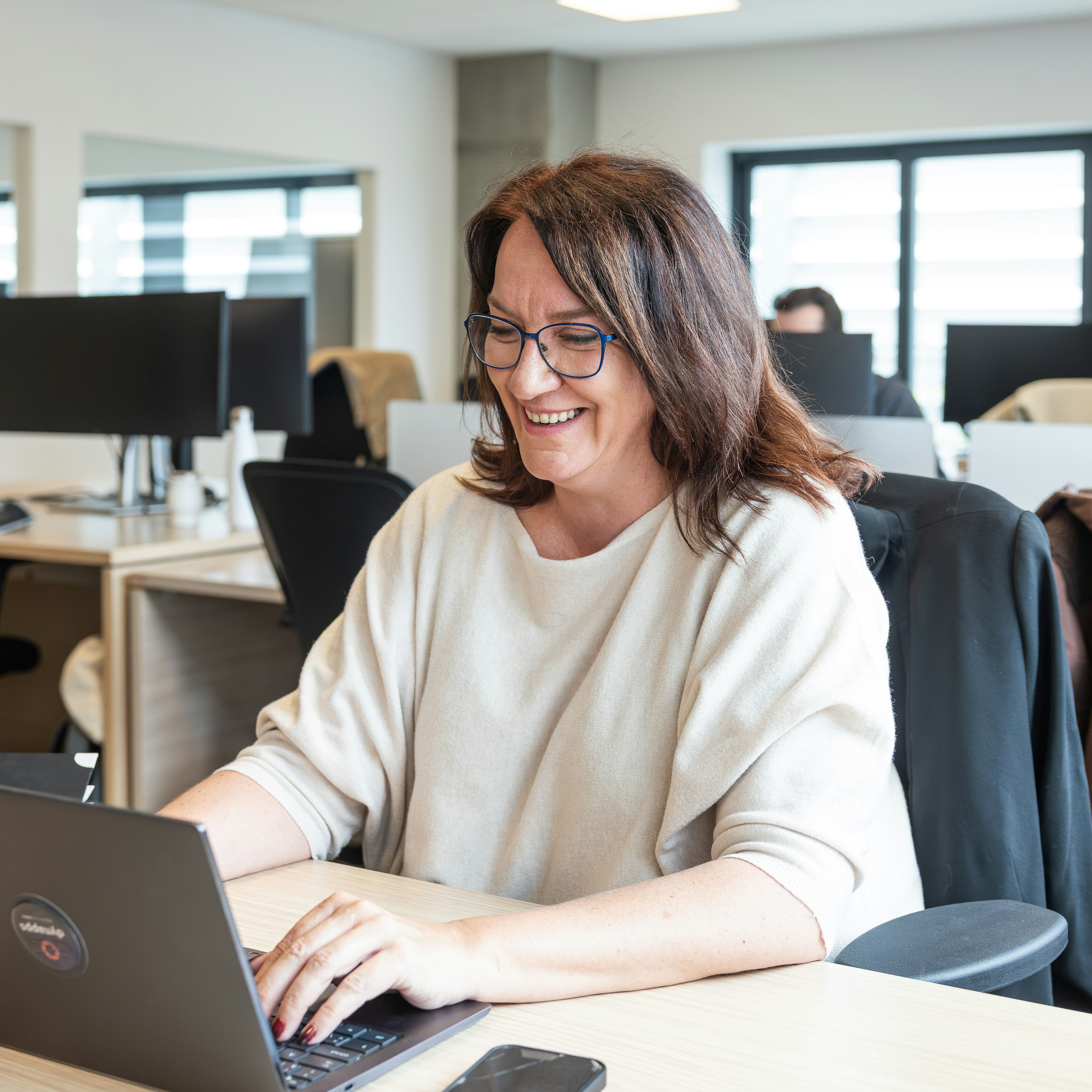 Smiling woman with glasses typing on a laptop