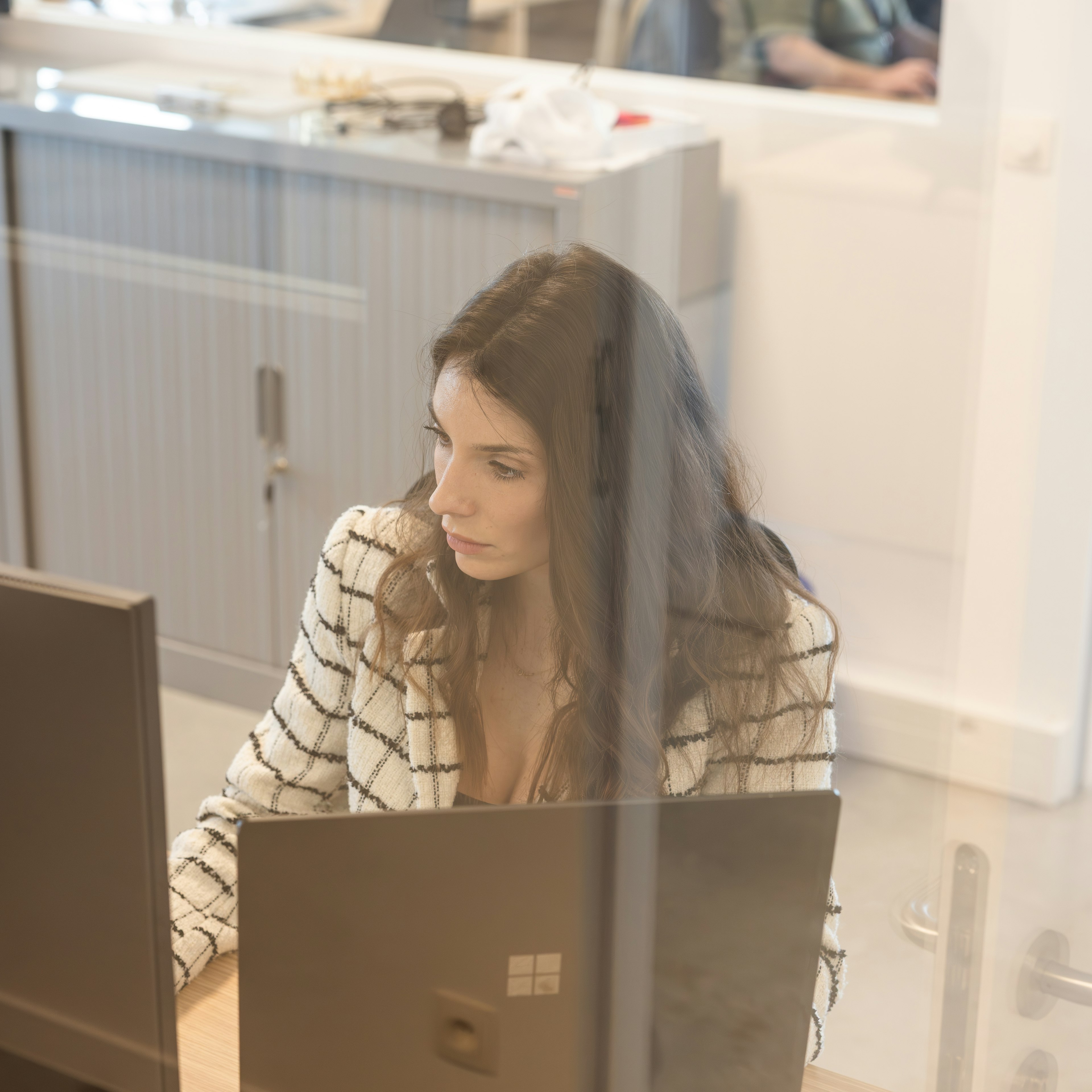 Woman concentrating on her laptop seen through office glass