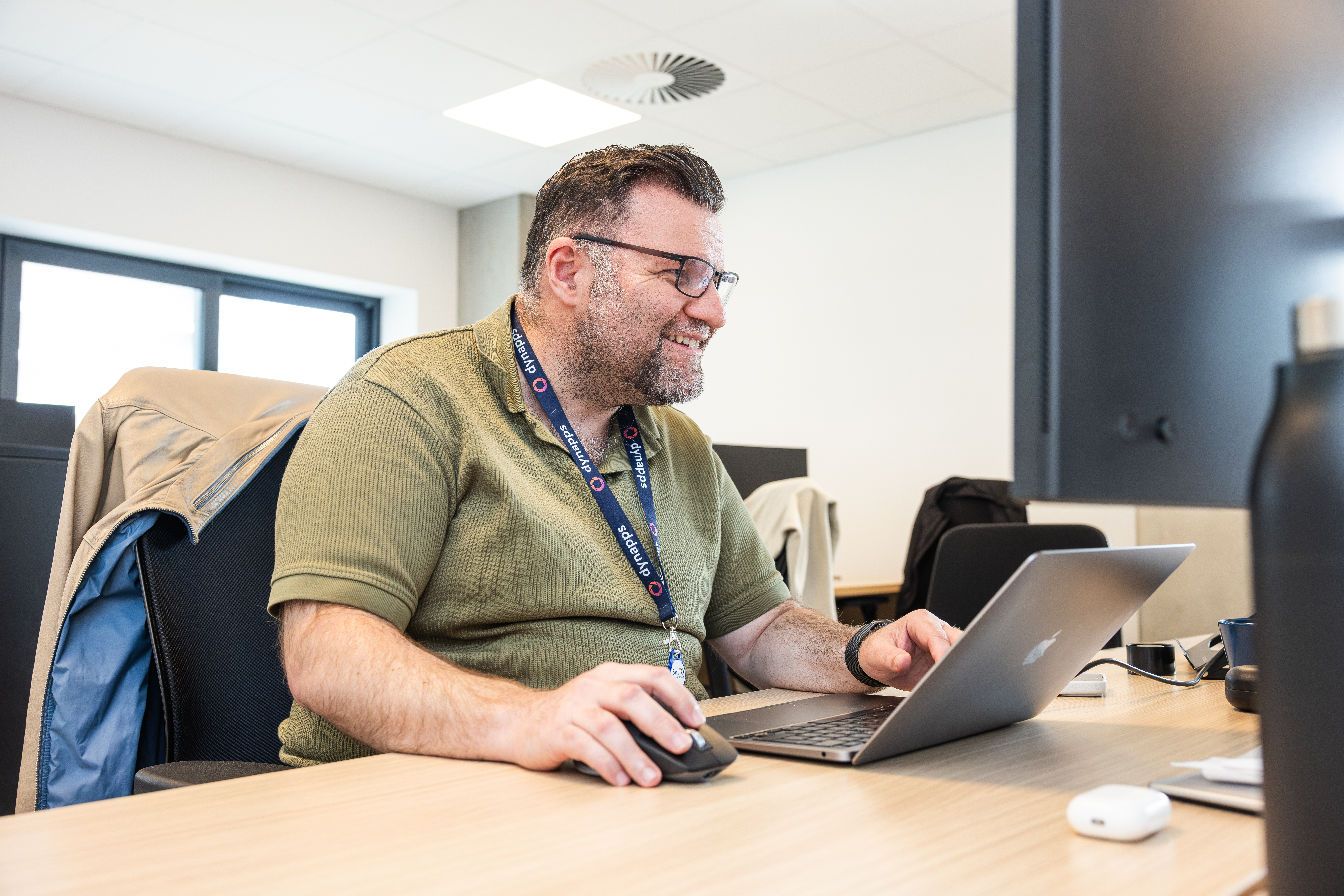 Smiling man with Dynapps lanyard using laptop and mouse