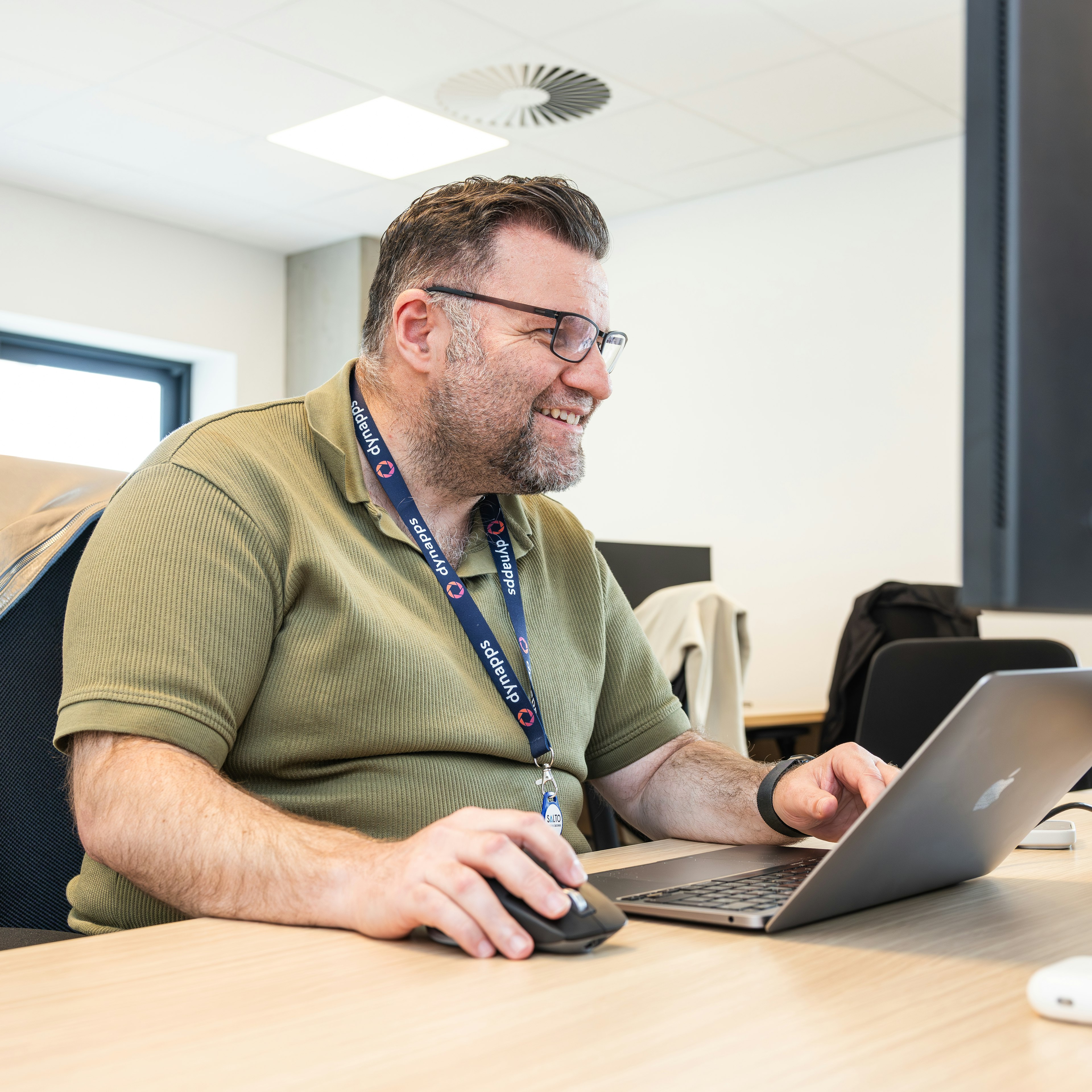 Smiling man with Dynapps lanyard using laptop and mouse
