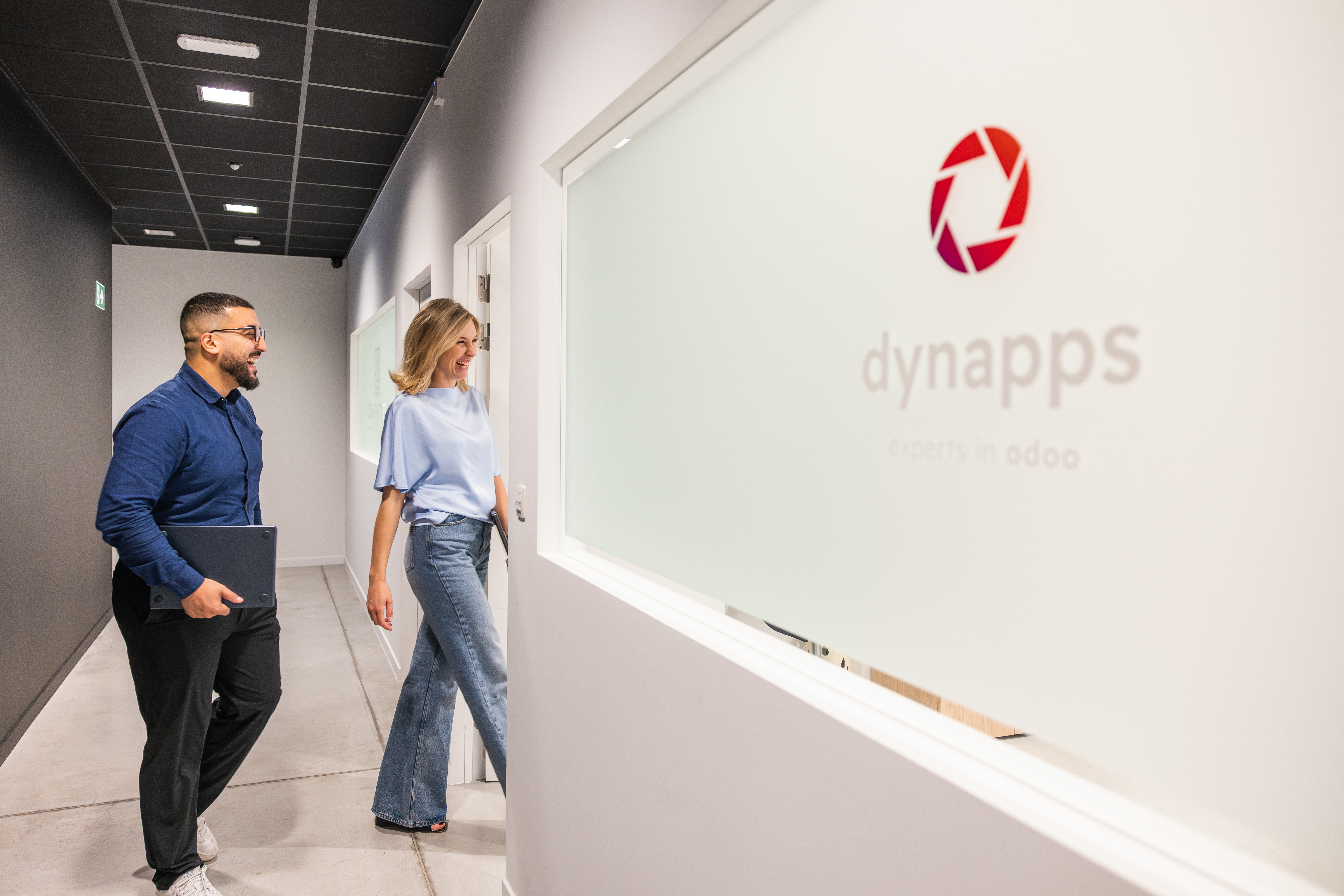 Deux collègues souriants passant devant le logo de Dynapps