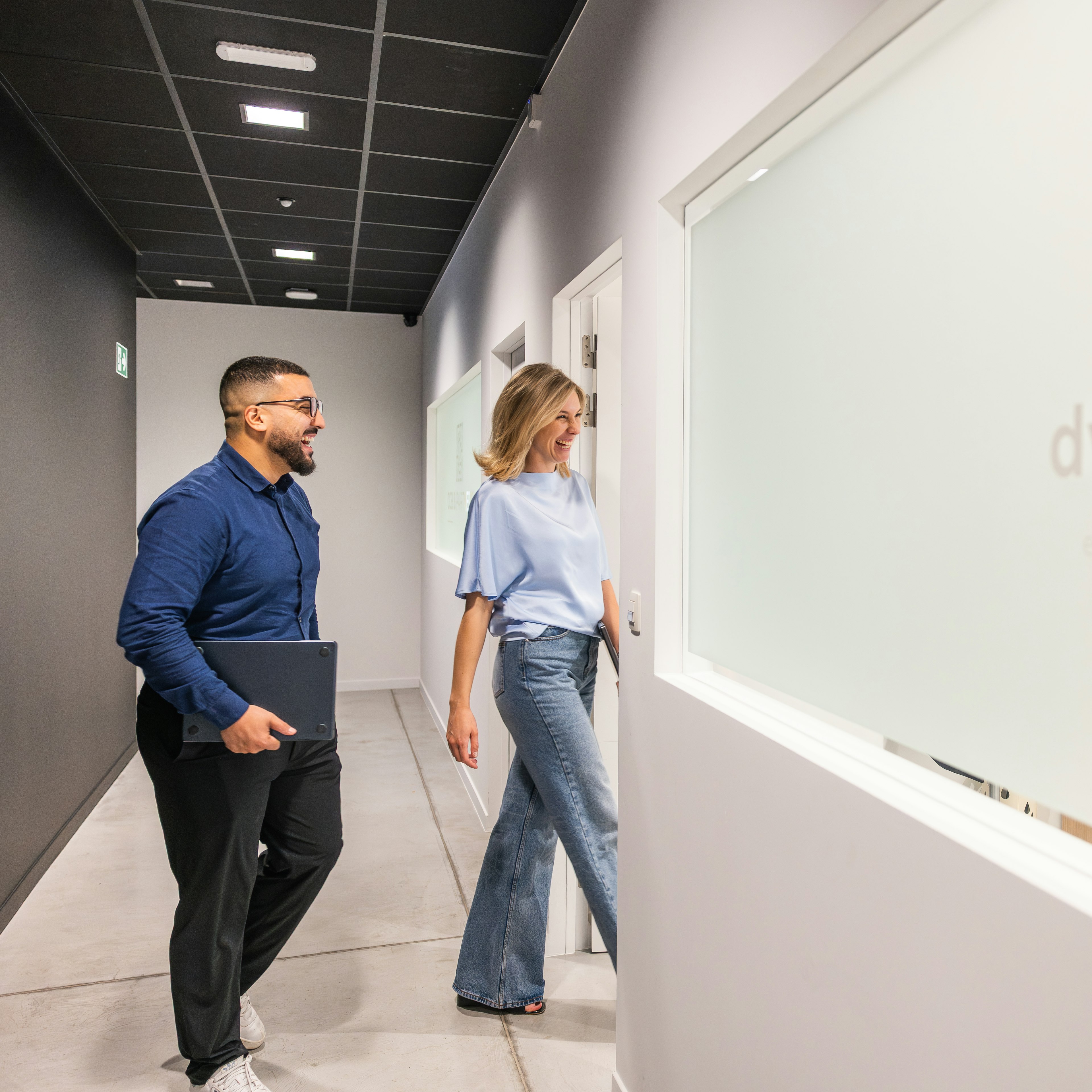 Two smiling colleagues walking past the Dynapps office logo