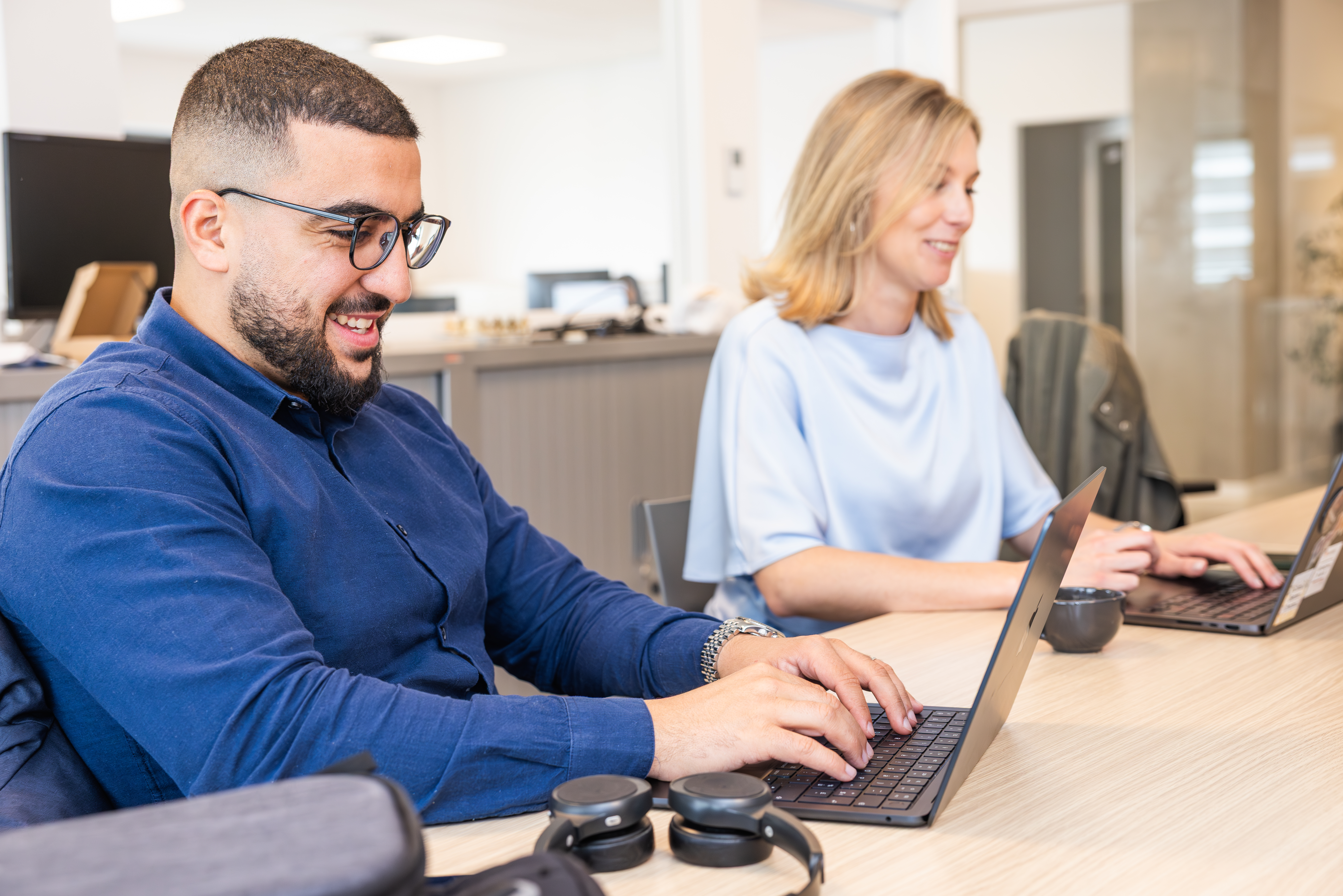 Un consultant souriant tapant sur un ordinateur portable dans un bureau en open space