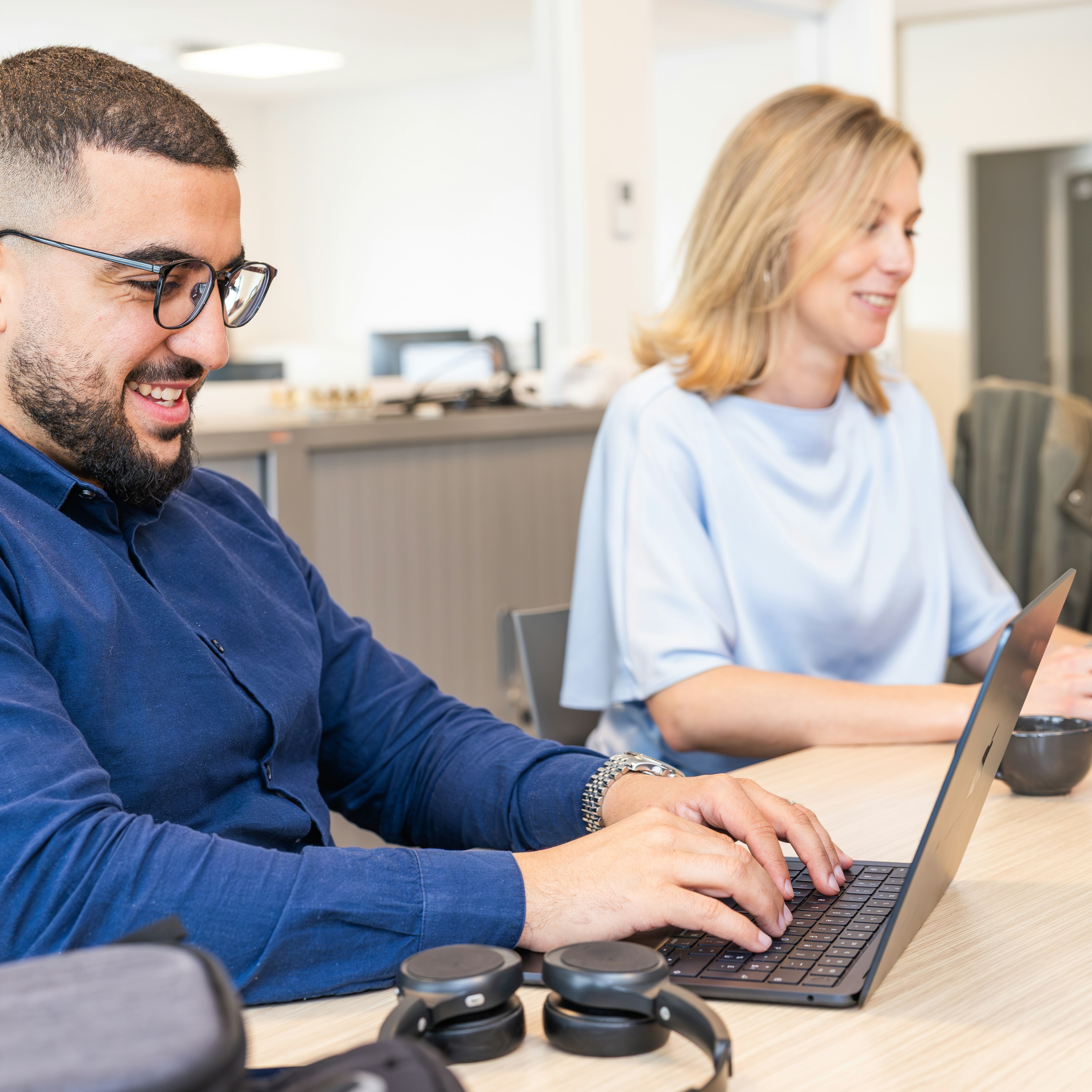 Un consultant souriant tapant sur un ordinateur portable dans un bureau en open space