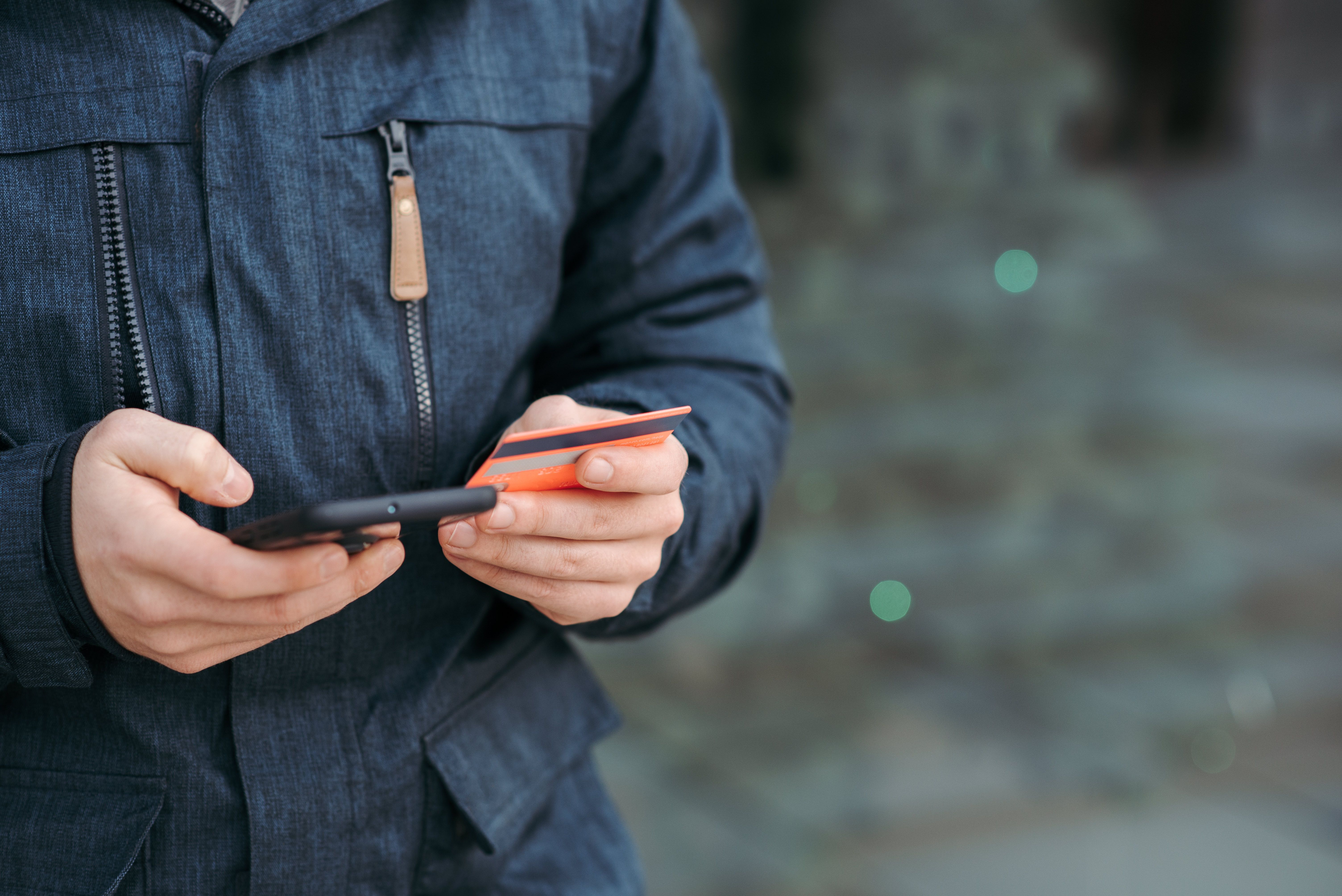 Hombre realizando un pago digital con tarjeta y smartphone en la calle.