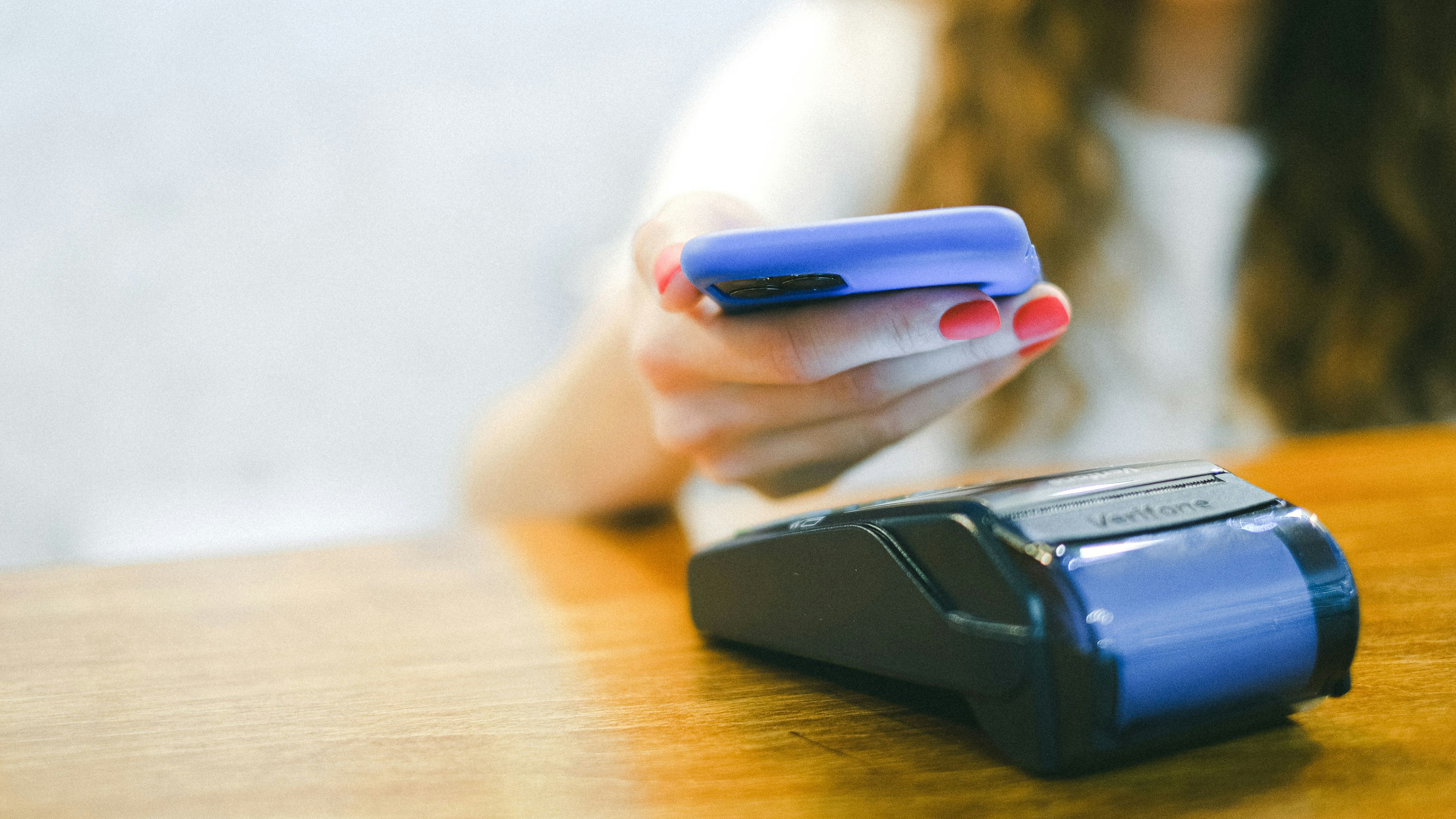 Primer plano de un pago móvil contactless mediante tecnología NFC utilizando un smartphone sobre un datáfono o terminal de tarjetas en un comercio.