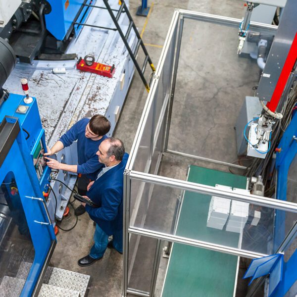 Vue aérienne de deux techniciens en train de manipuler le panneau de commande d'une grande machine de production bleue dans une usine.