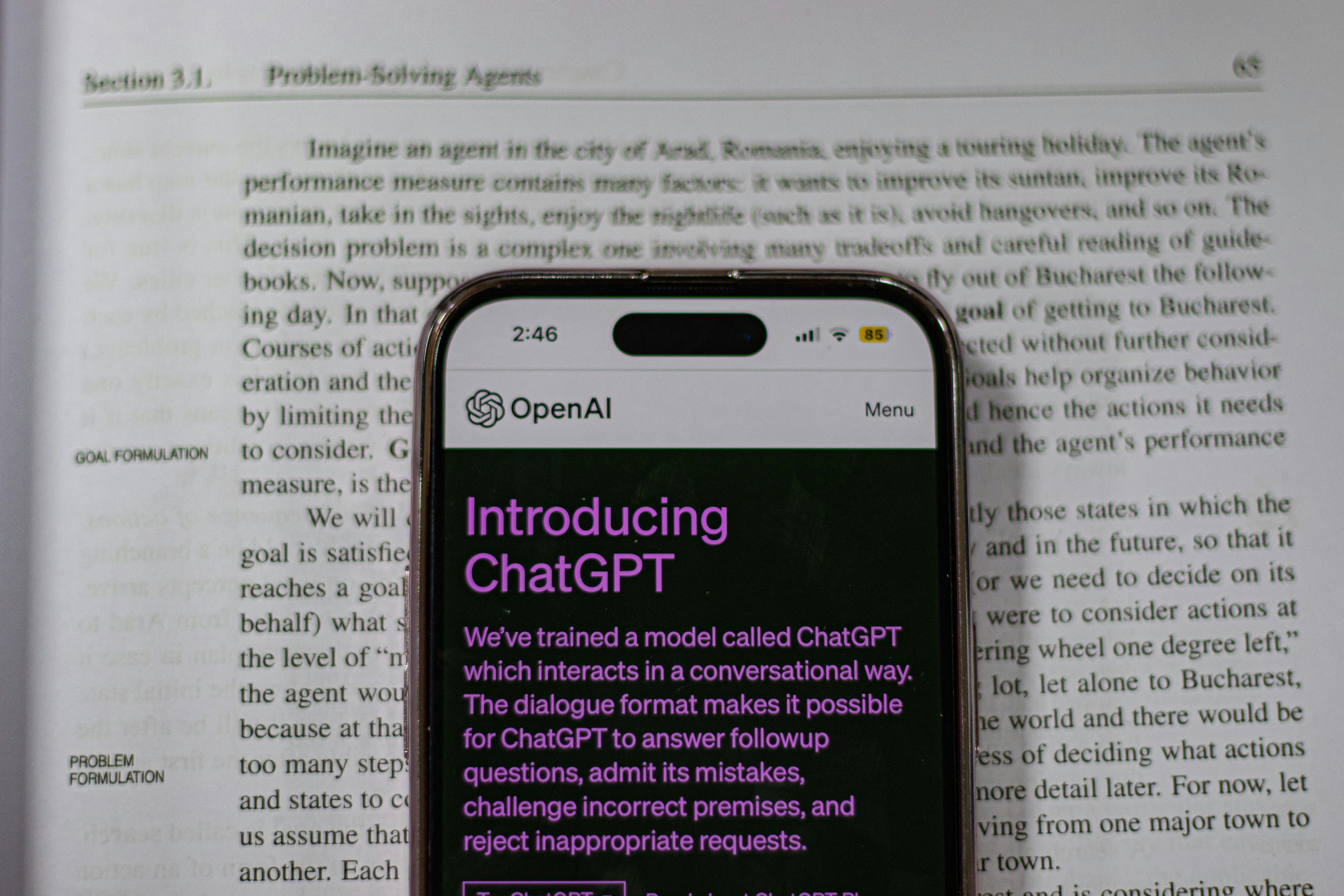 This image shows a smartphone displaying the OpenAI webpage titled "Introducing ChatGPT," placed over an open textbook page discussing "Section 3.1. Problem-Solving Agents" in artificial intelligence.