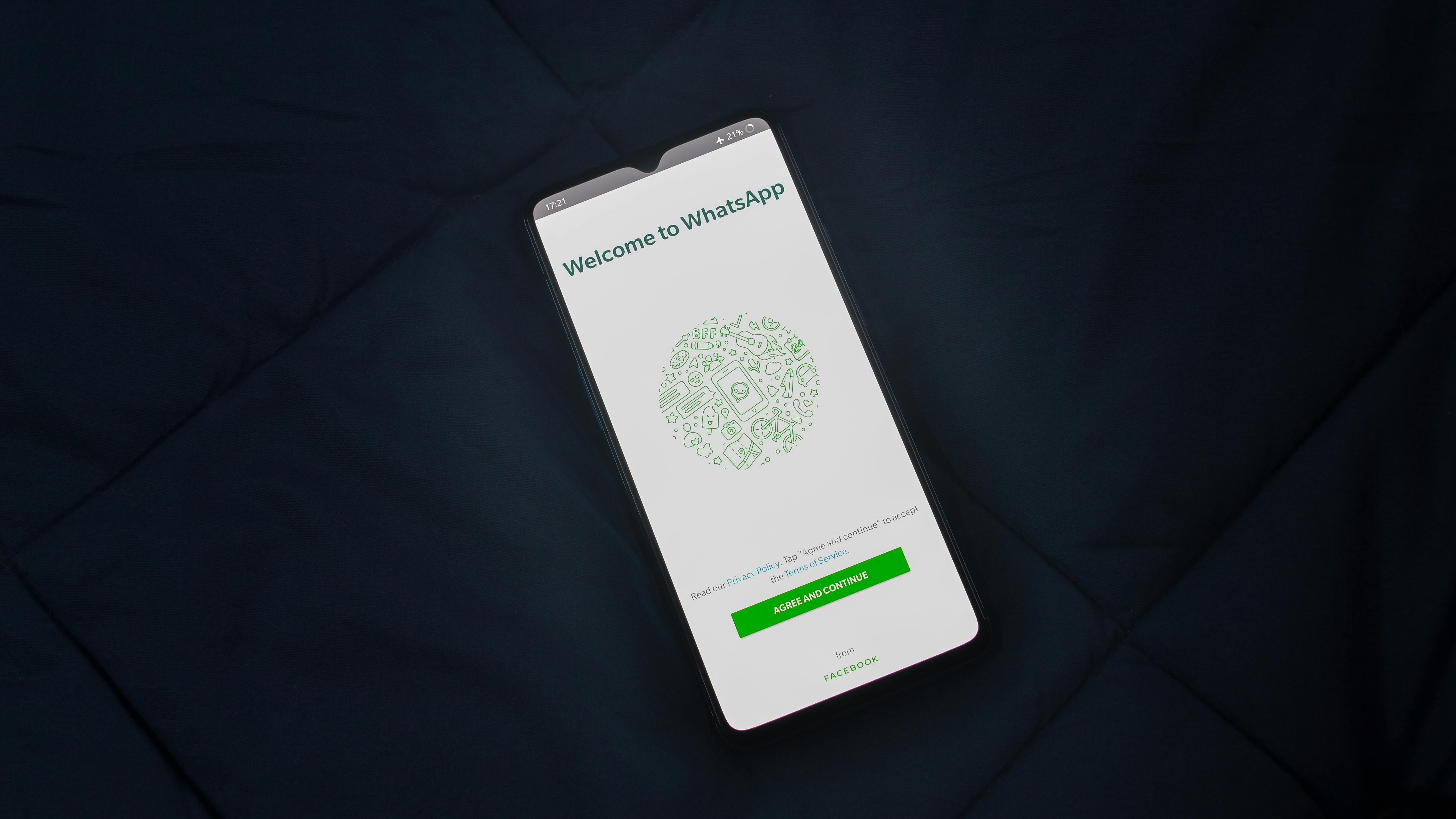 This image shows a smartphone resting on a dark fabric surface, displaying the initial setup screen for the WhatsApp application with the text "Welcome to WhatsApp" and an "AGREE AND CONTINUE" button.