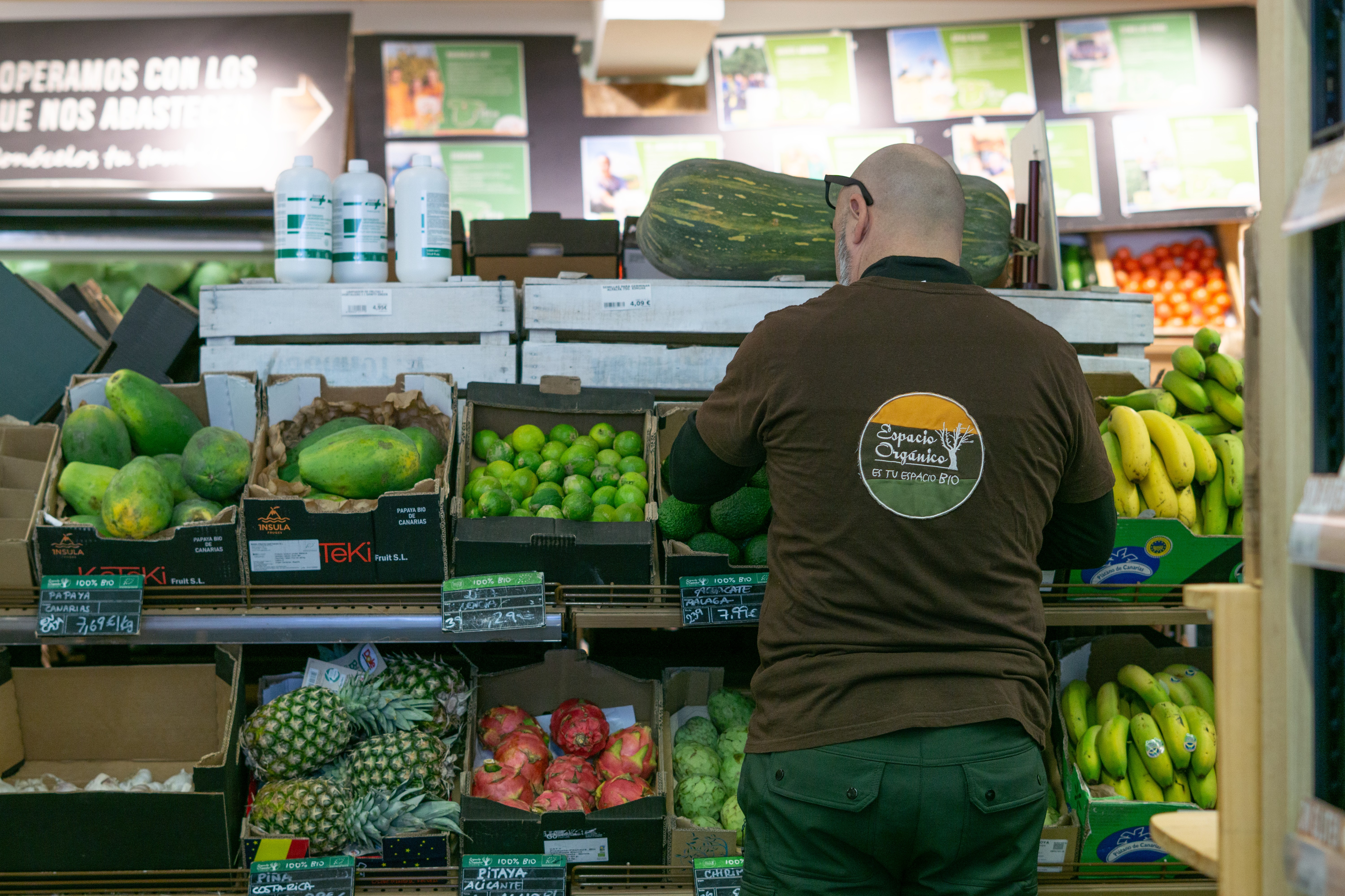 Un employé d'Espacio Orgánico, vêtu d'un polo aux couleurs de l'enseigne, range les fruits et légumes bio exposés, notamment des papayes, des citrons verts, des ananas et des bananes, dans des caisses.