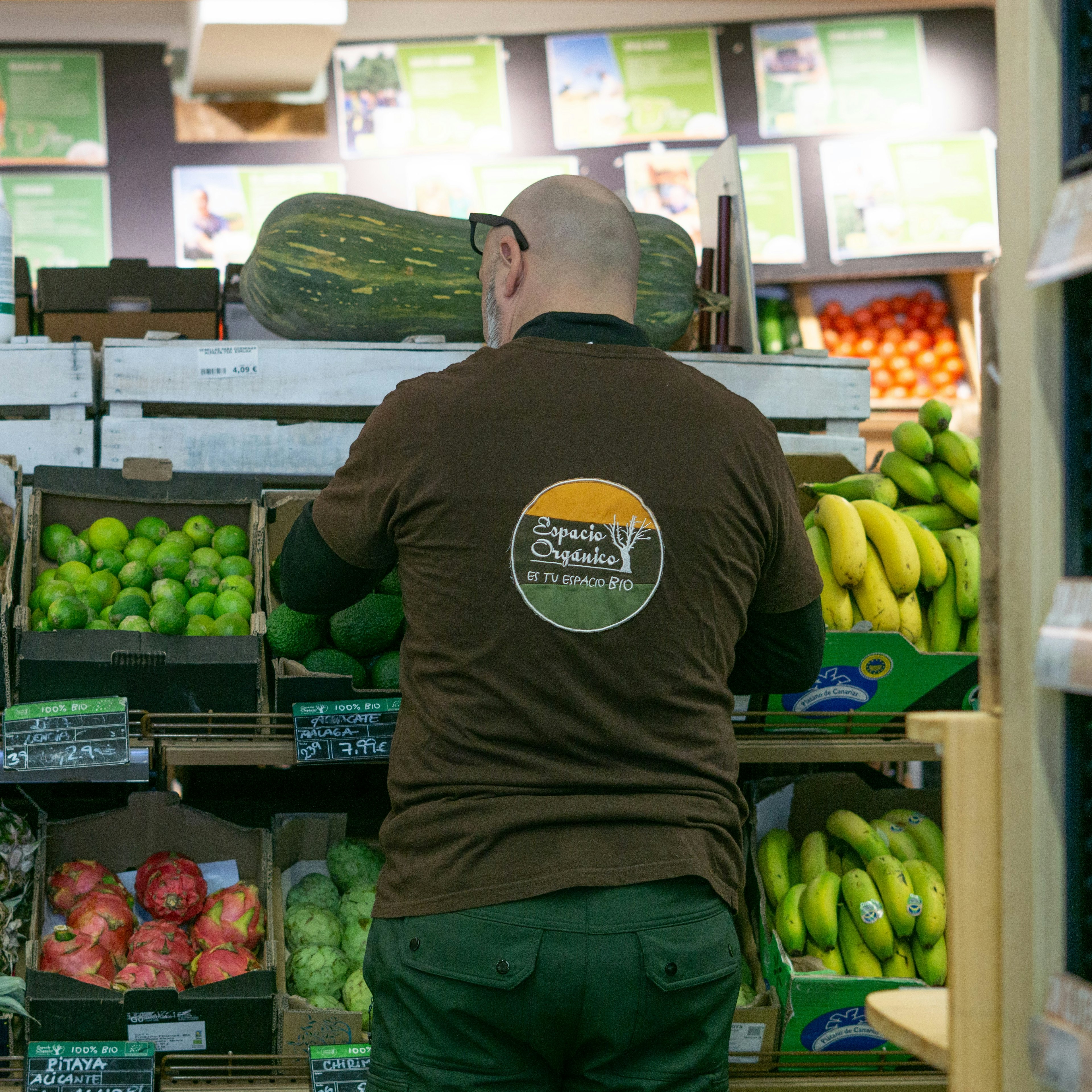 Un employé d'Espacio Orgánico, vêtu d'un polo aux couleurs de l'enseigne, range les fruits et légumes bio exposés, notamment des papayes, des citrons verts, des ananas et des bananes, dans des caisses.