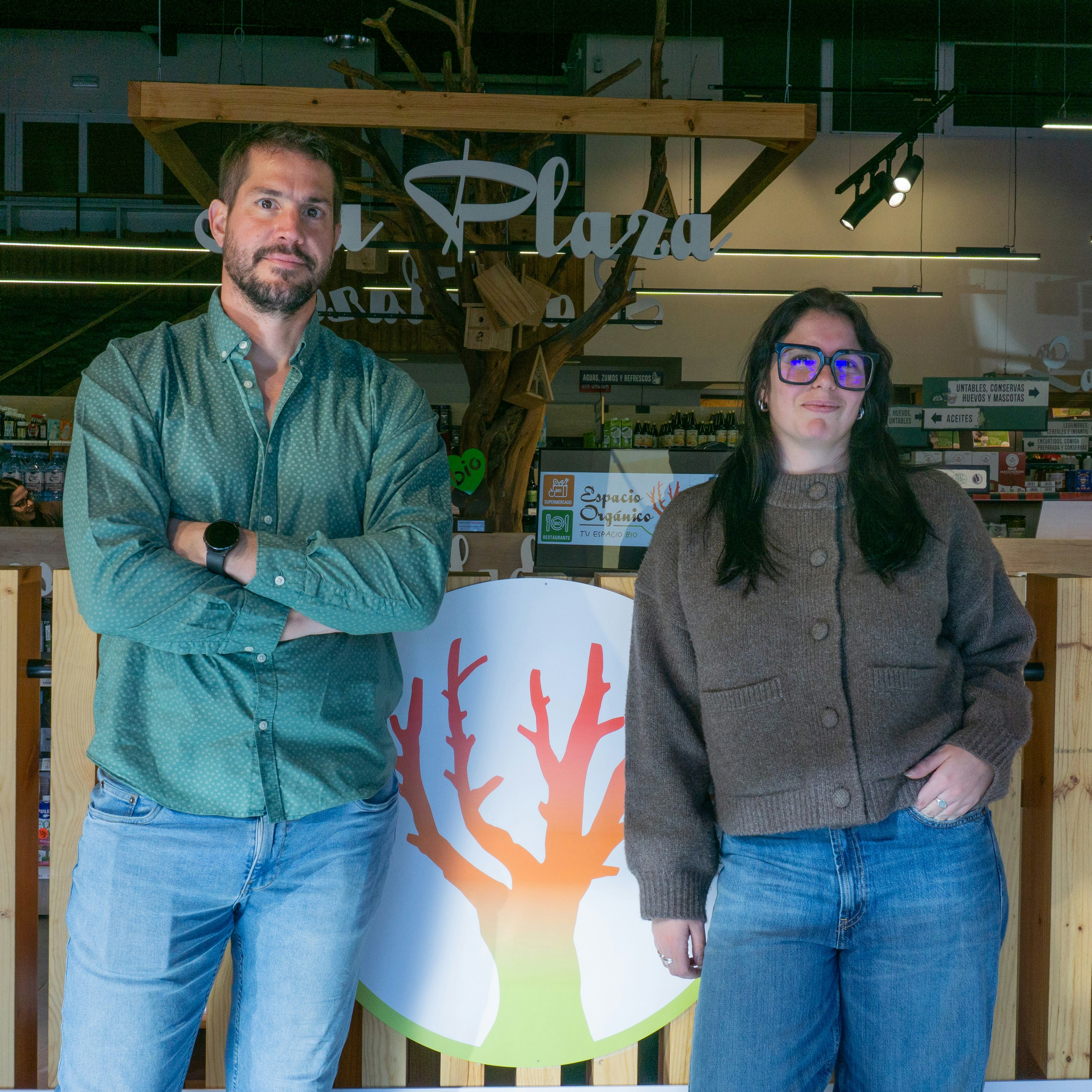 Un homme et une femme se tiennent de part et d'autre du logo en forme d'arbre d'Espacio Orgánico, à l'entrée du supermarché bio.