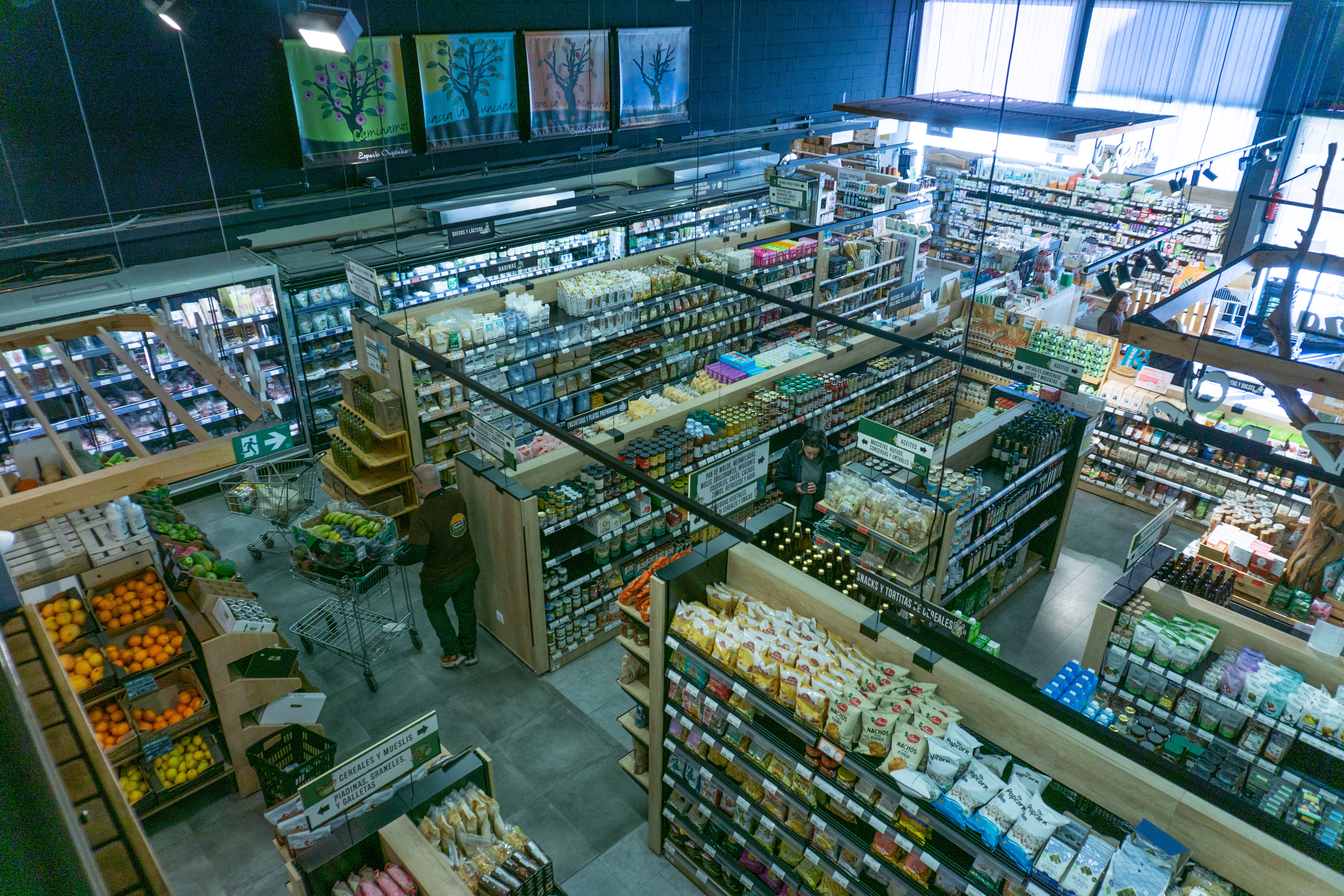 Vue aérienne du magasin Espacio Orgánico, montrant des caisses de fruits et légumes, des rayons bien approvisionnés et des bannières publicitaires au-dessus des étagères.