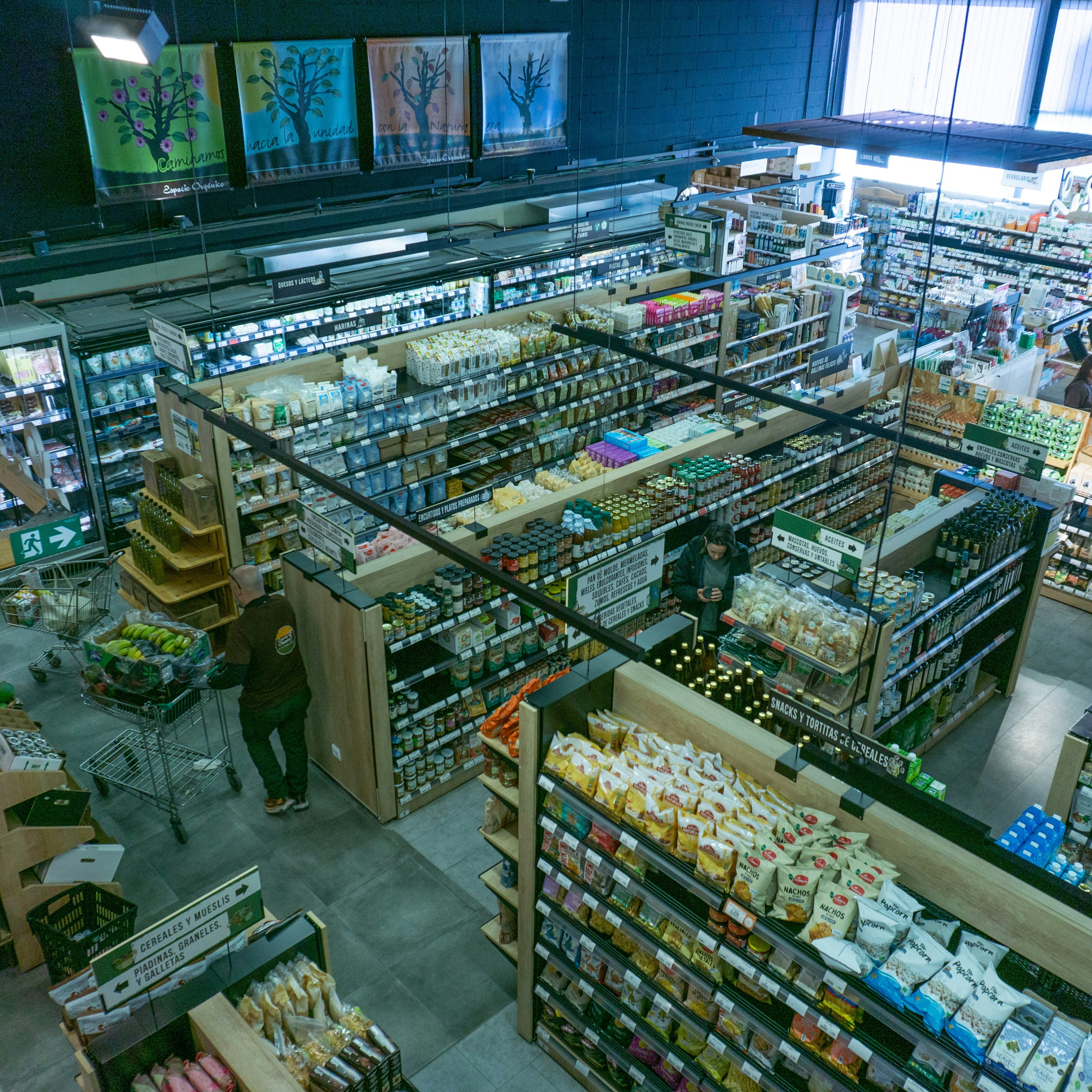 Vue aérienne du magasin Espacio Orgánico, montrant des caisses de fruits et légumes, des rayons bien approvisionnés et des bannières publicitaires au-dessus des étagères.