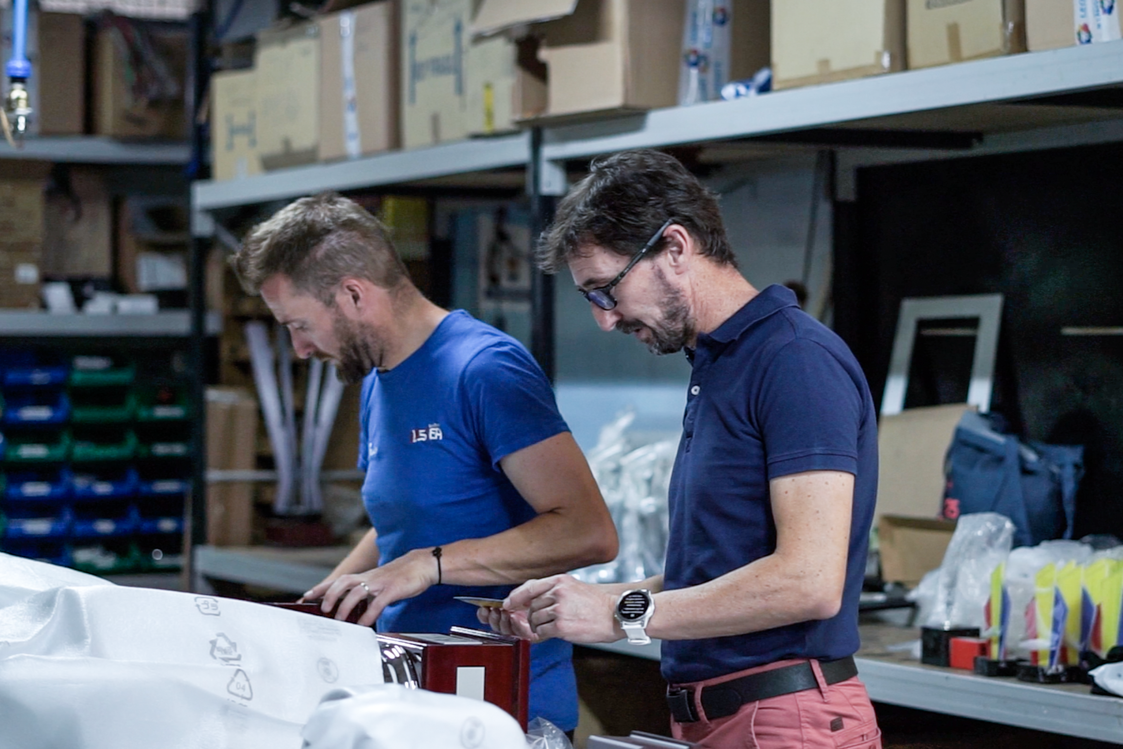 Two Todotrofeo workers pack finished products at a bench in the warehouse, with stocked shelves and bins behind them.