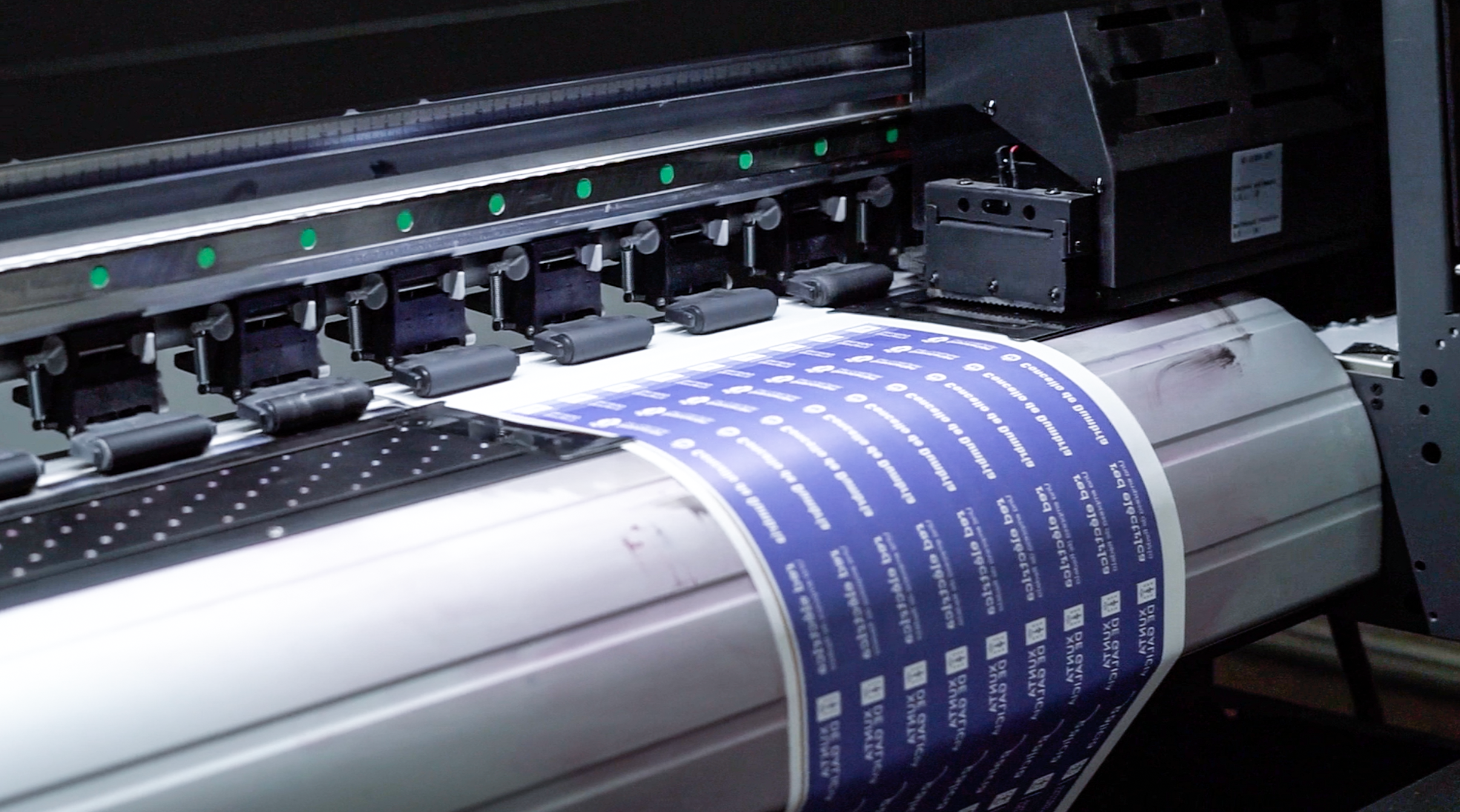 A wide-format printer feeds a roll of material printing a repeating blue design across the sheet.