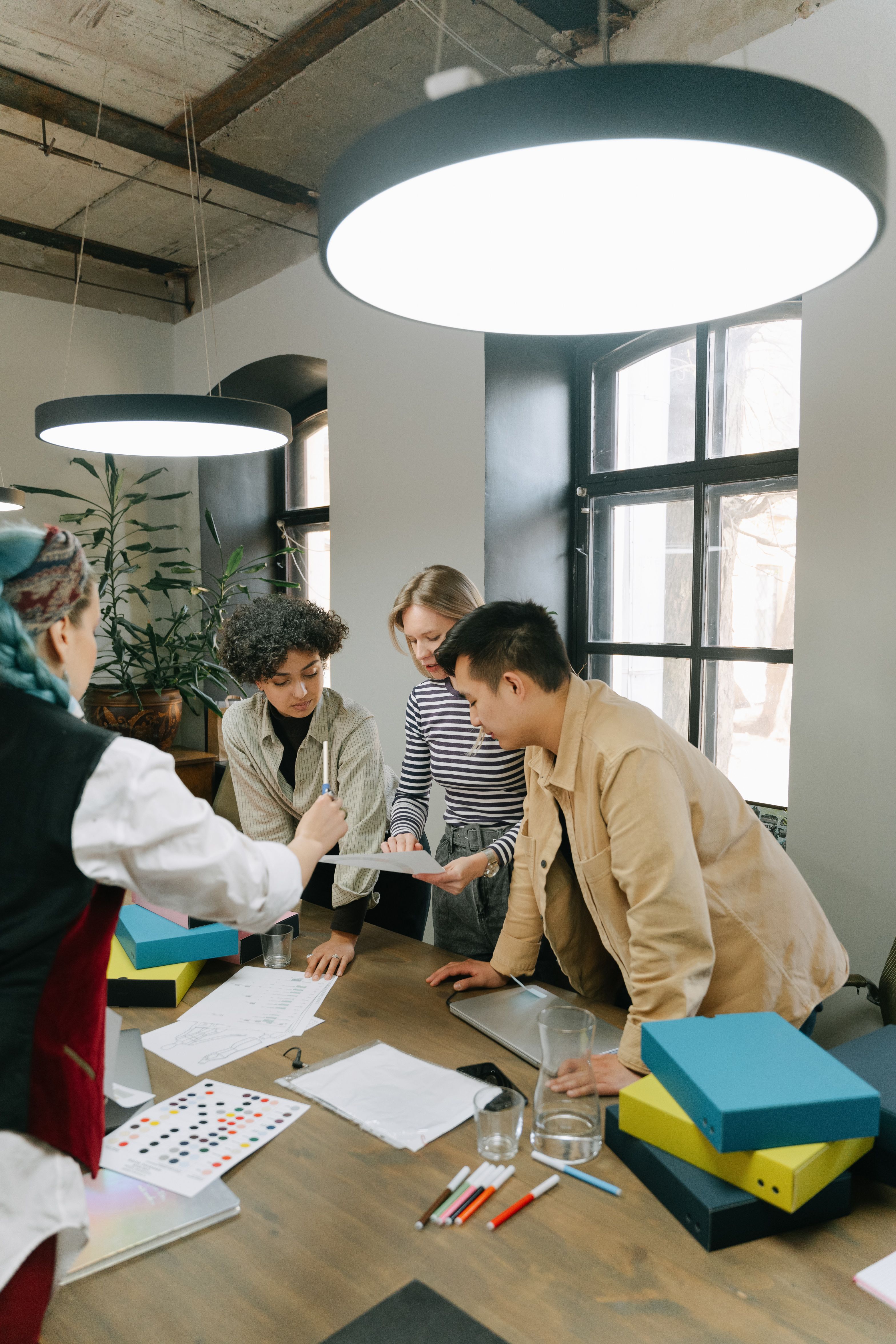 A team reviews design samples, colour swatches and boxes around a table in a creative studio.