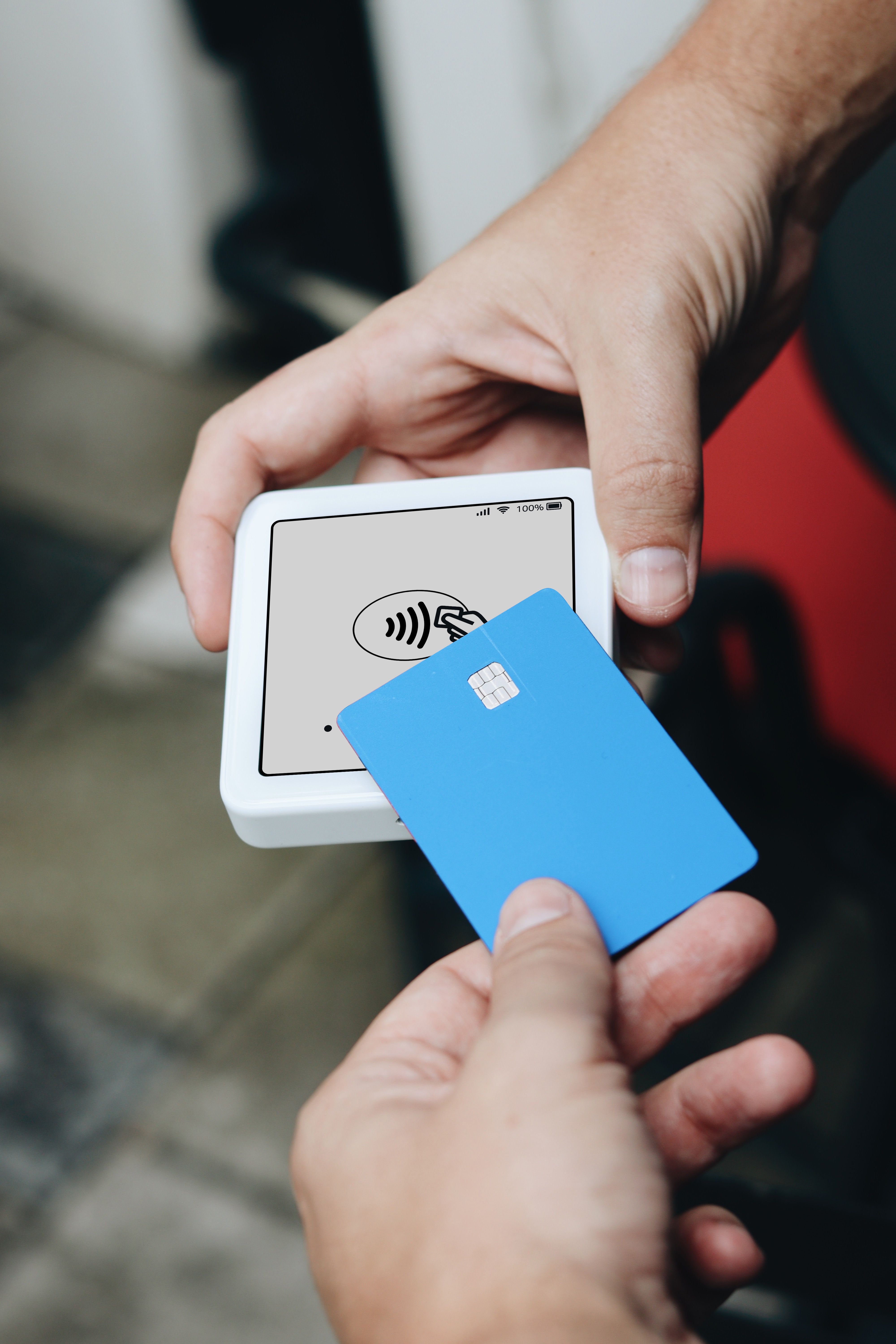 A customer taps a blue contactless card on a white card reader held by a vendor to make a payment.