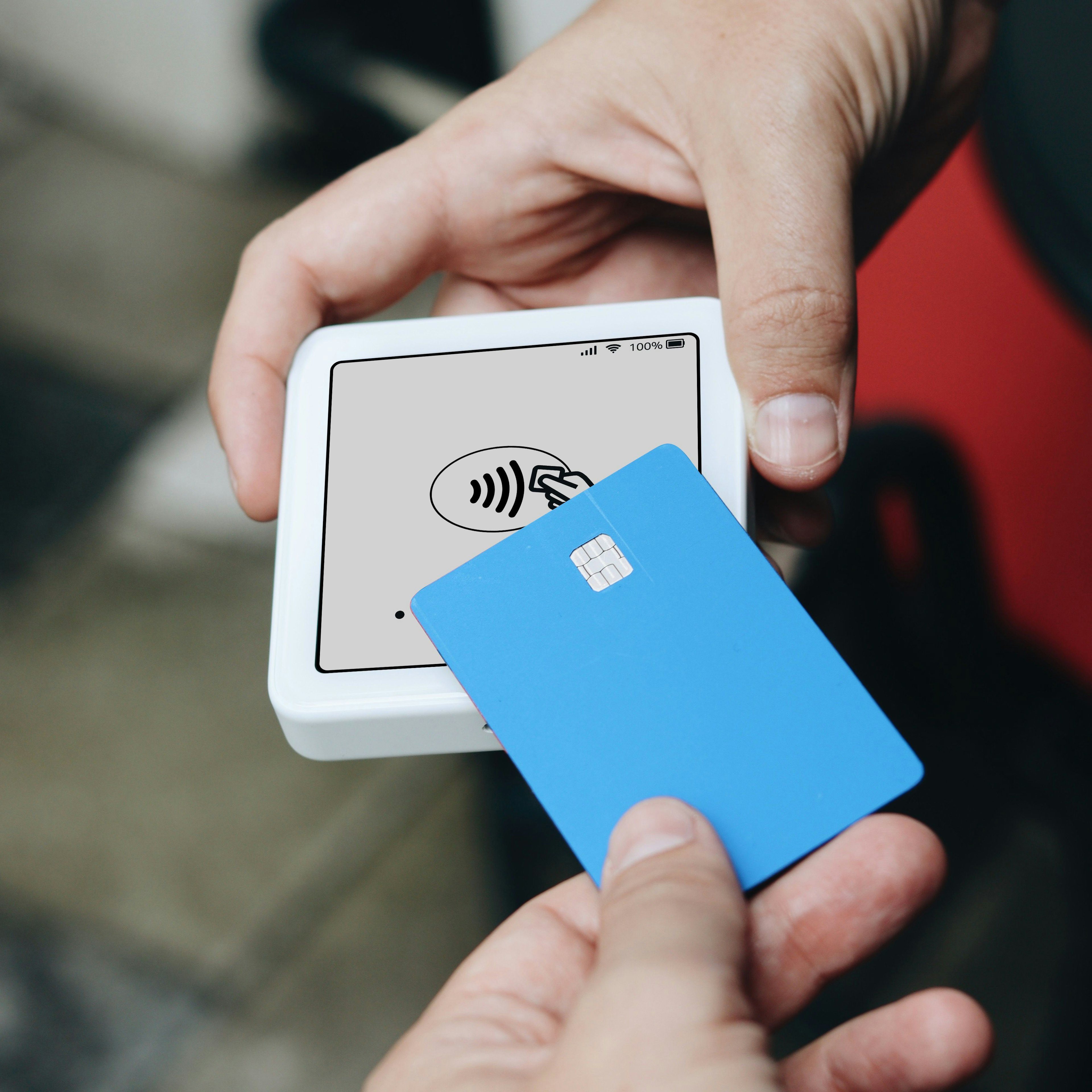 Un client approche une carte sans contact bleue d'un lecteur de carte blanc tenu par un vendeur pour effectuer un paiement.