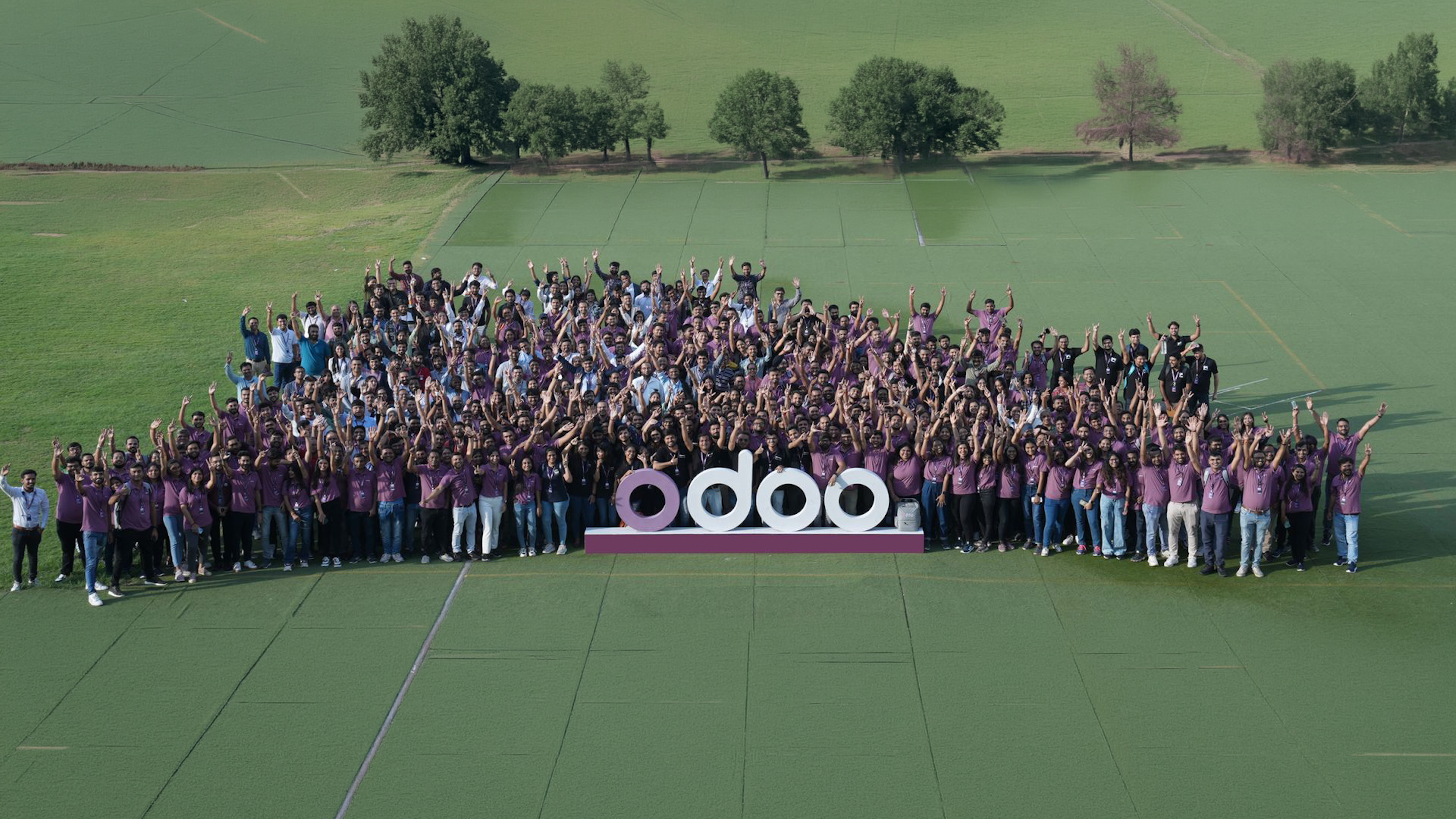 a group of more than 100 people surrounding the Odoo logo