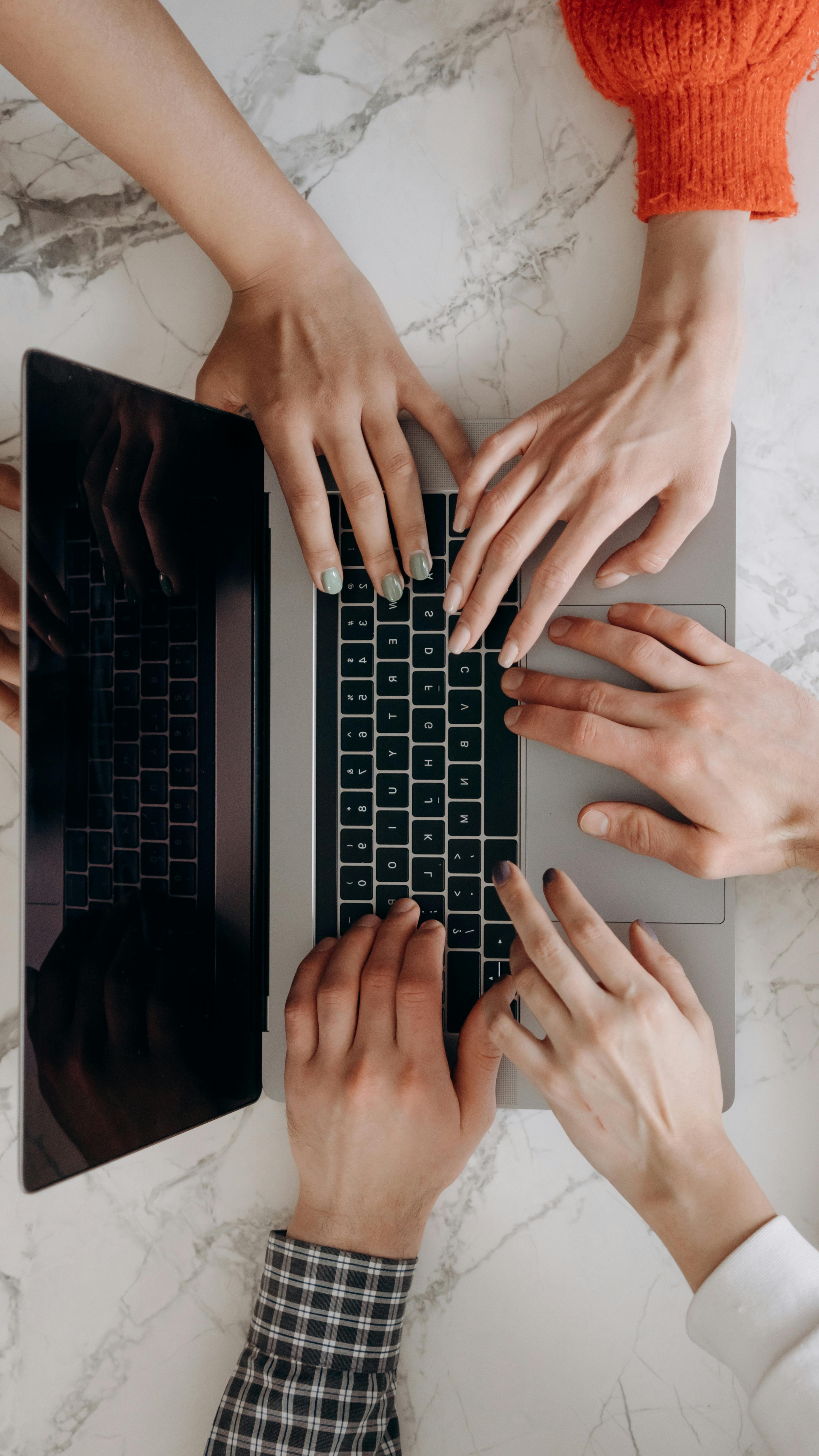 Múltiples manos de un equipo trabajando juntas en el teclado de una computadora portátil, simbolizando colaboración y trabajo en equipo.