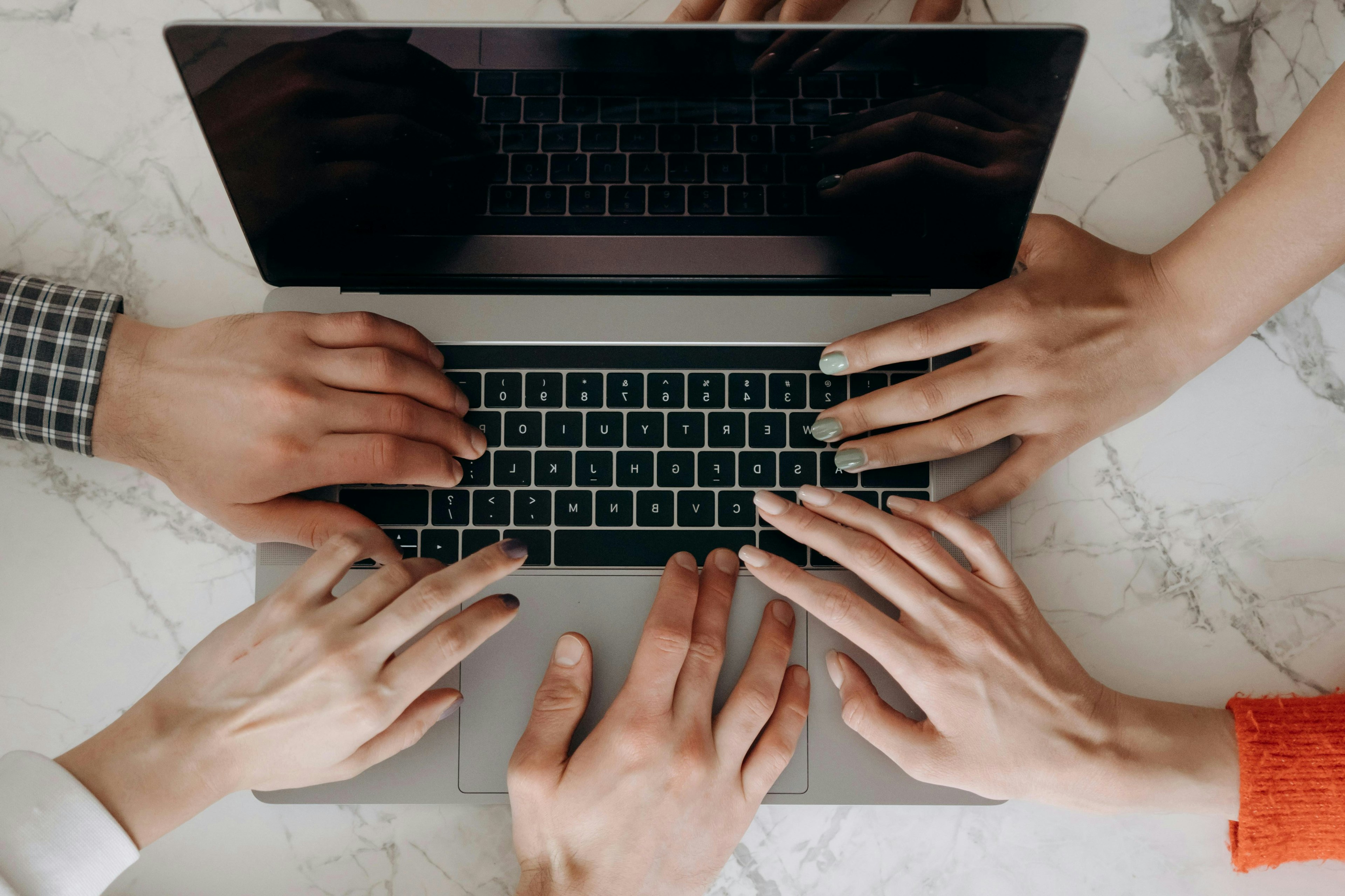 Múltiples manos de un equipo trabajando juntas en el teclado de una computadora portátil, simbolizando colaboración y trabajo en equipo.