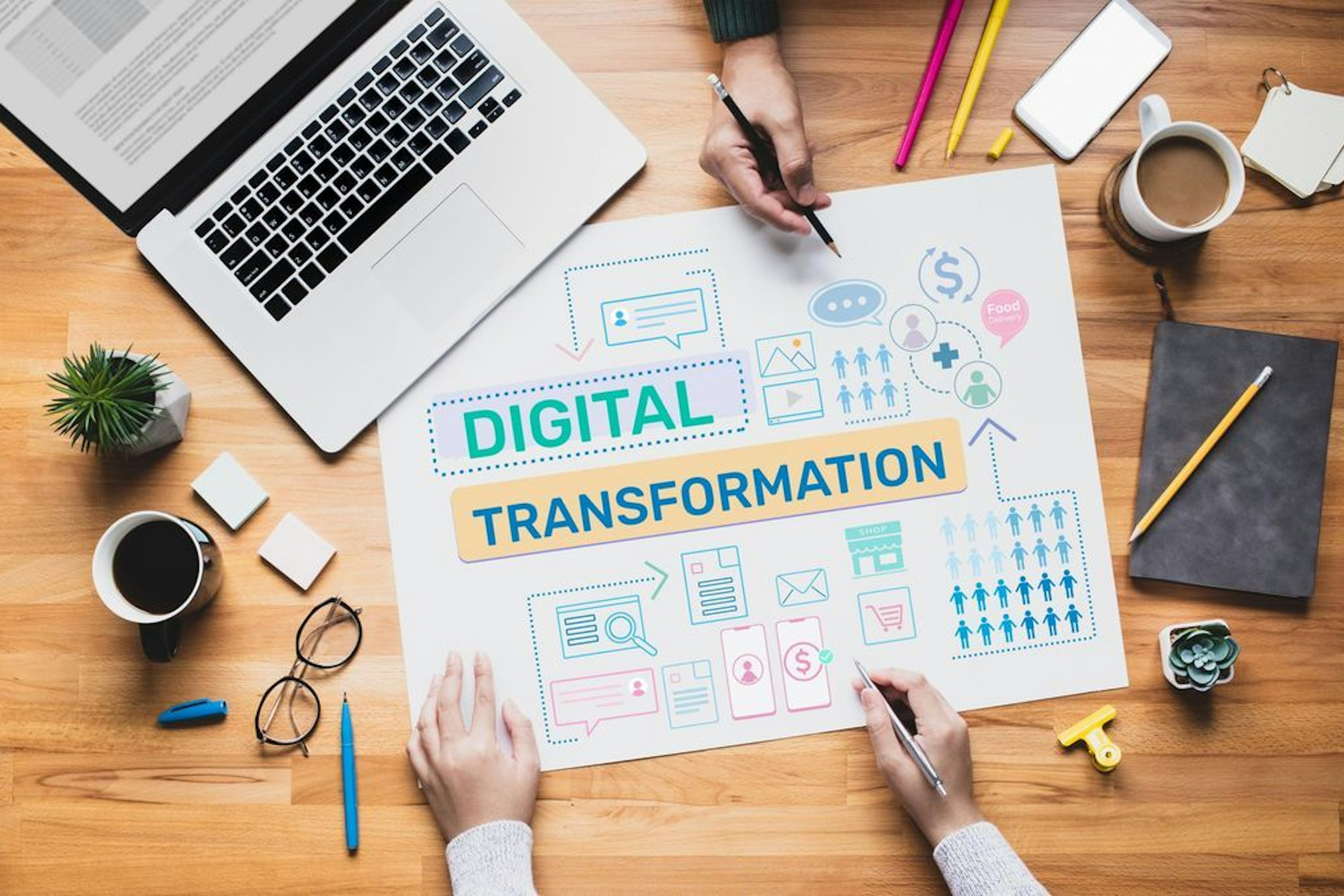 Dos personas trabajando en un proyecto de transformación digital, rodeadas de diagramas, iconos y elementos de oficina en un escritorio de madera.