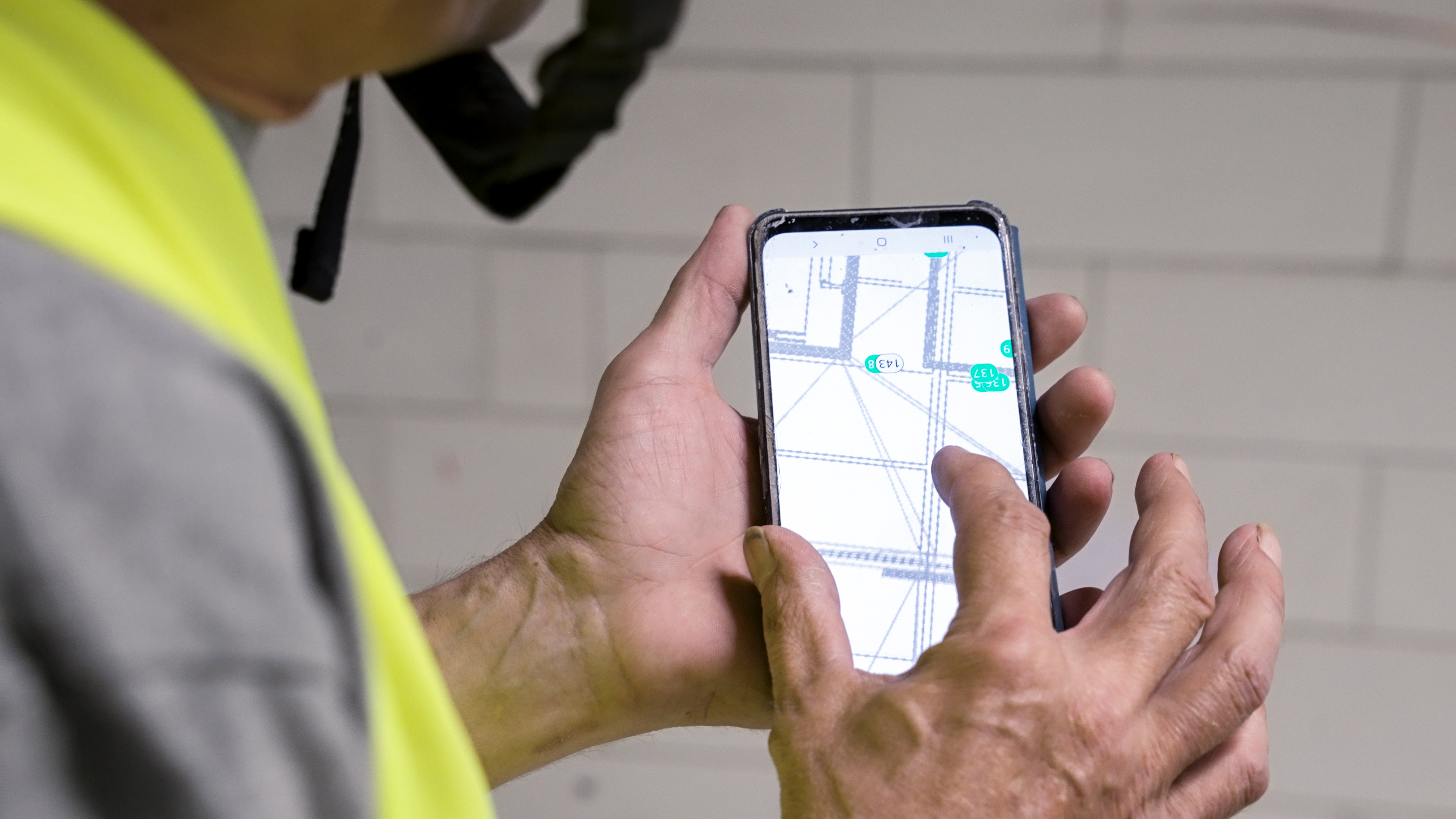 Close-up of a Fire System technician viewing an annotated floor plan with tagged markers on a phone on site.