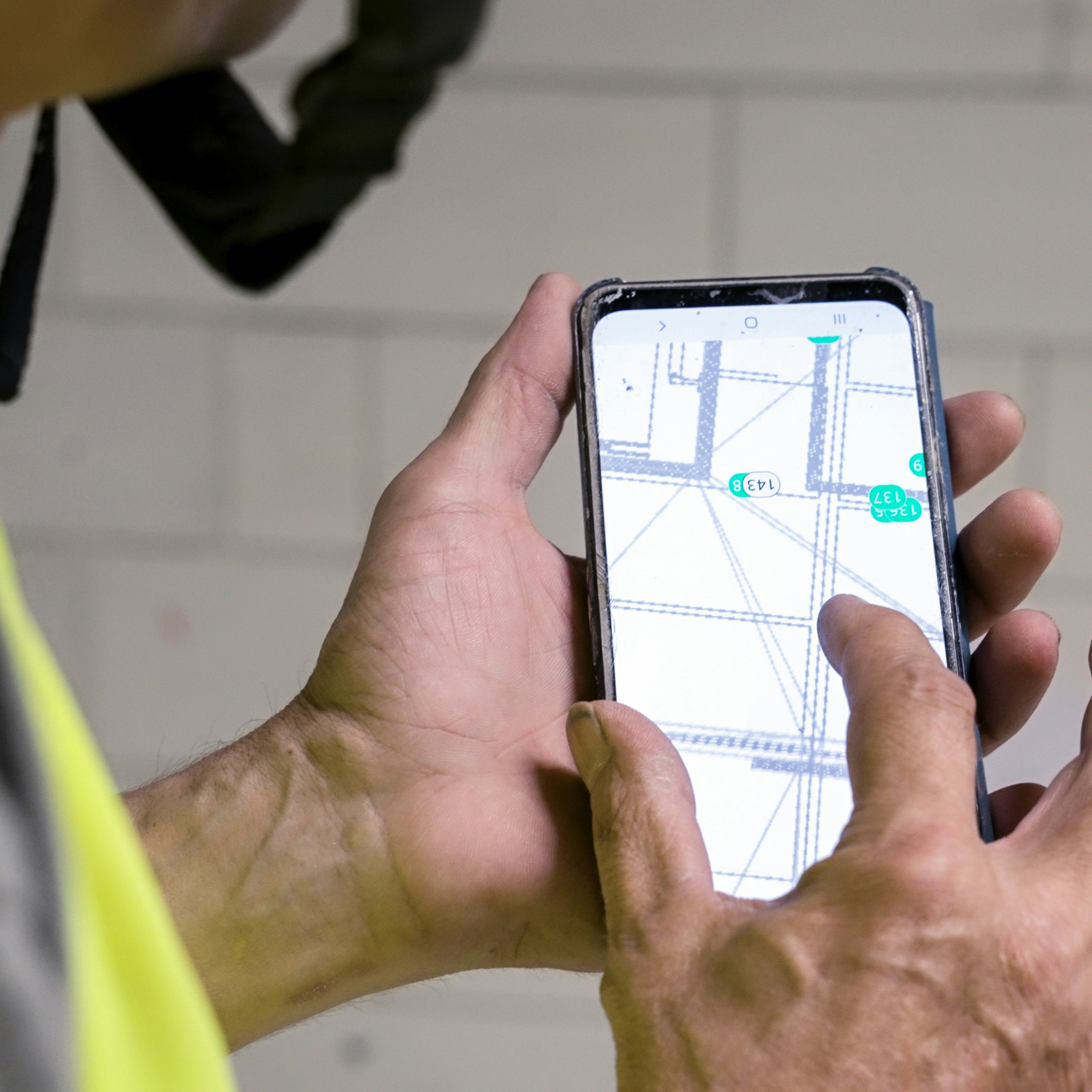 Gros plan sur un technicien spécialisé dans les systèmes d'extinction d'incendie consultant sur place, sur son téléphone, un plan d'étage annoté et muni de repères.