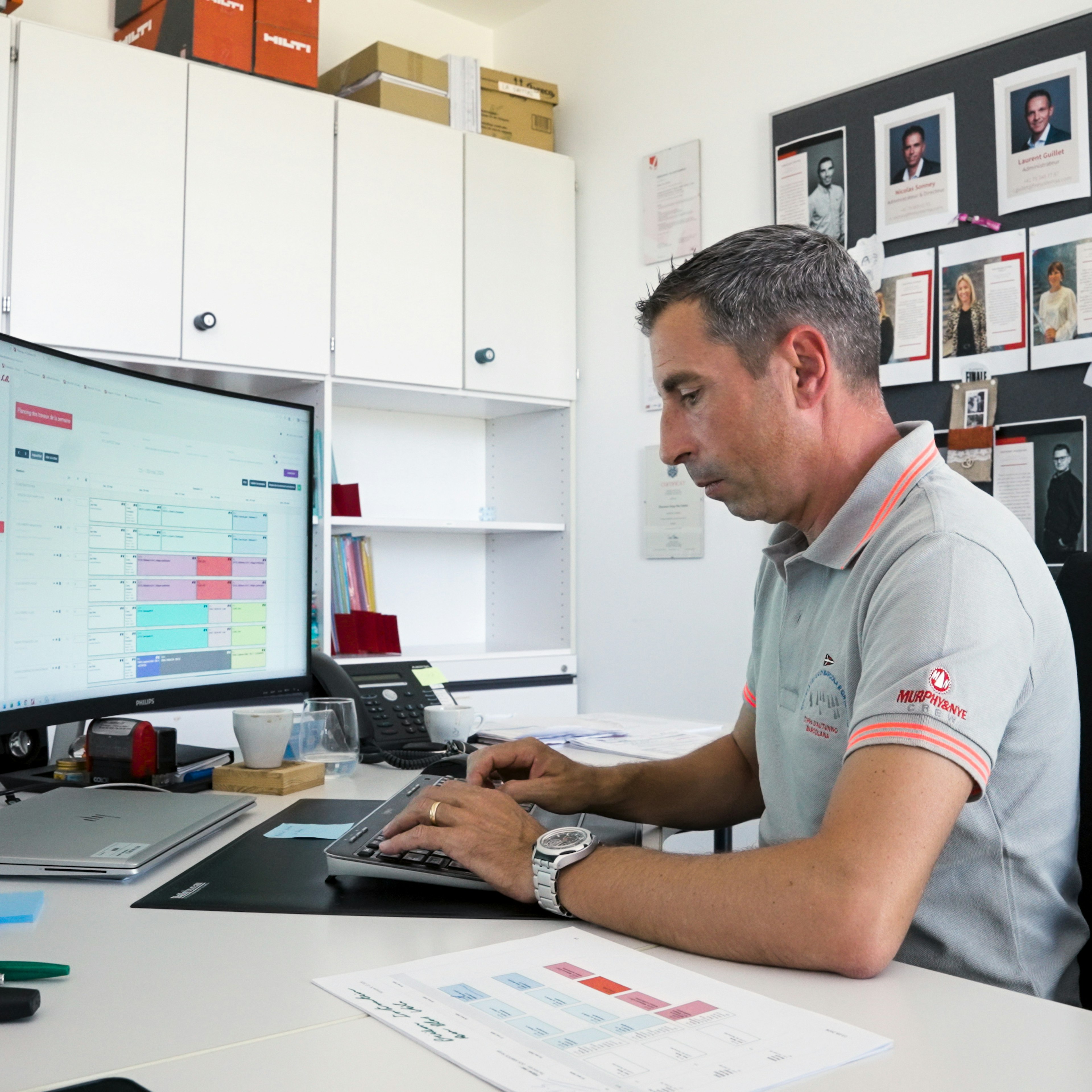 Un homme vêtu d'un polo Fire System travaille devant un bureau équipé de deux écrans, en train de consulter l'outil de planification FS Gestion sur un écran incurvé.