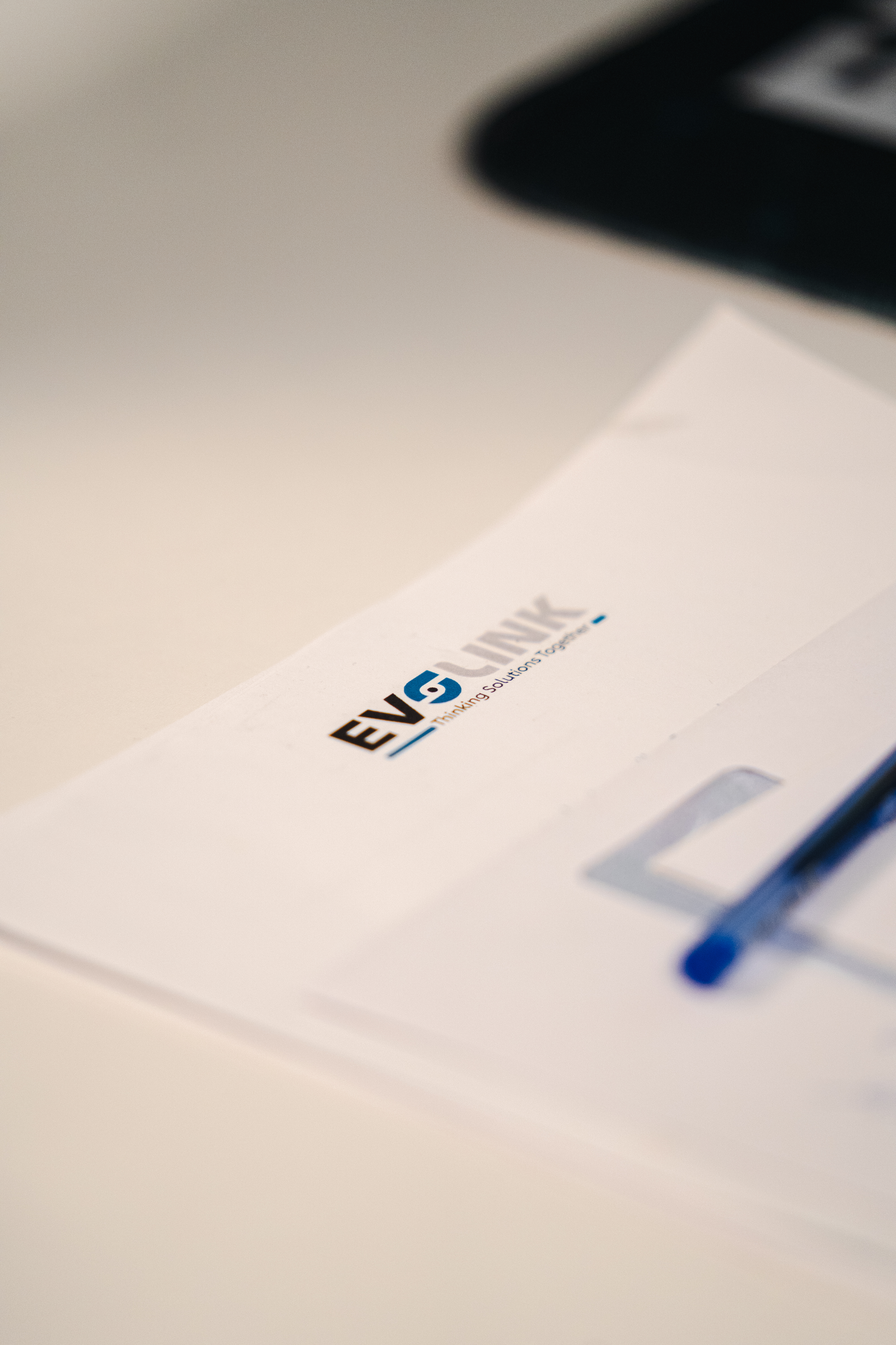 Close-up of an Evolink document on a desk showing the company logo and the tagline "Thinking Solutions Together", with a pen beside it.