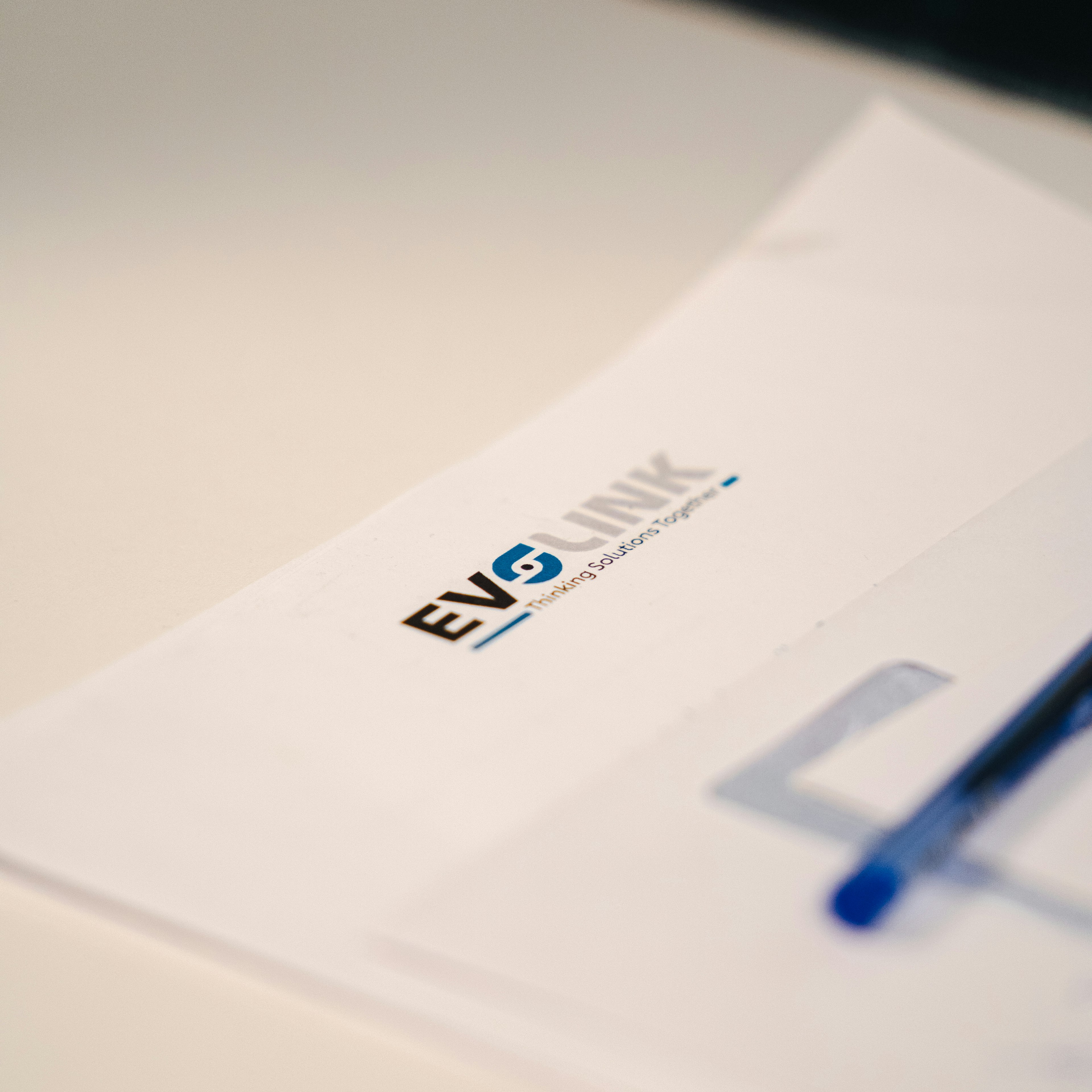 Gros plan sur un document Evolink posé sur un bureau, sur lequel figurent le logo de l'entreprise et le slogan « Thinking Solutions Together », avec un stylo à côté.