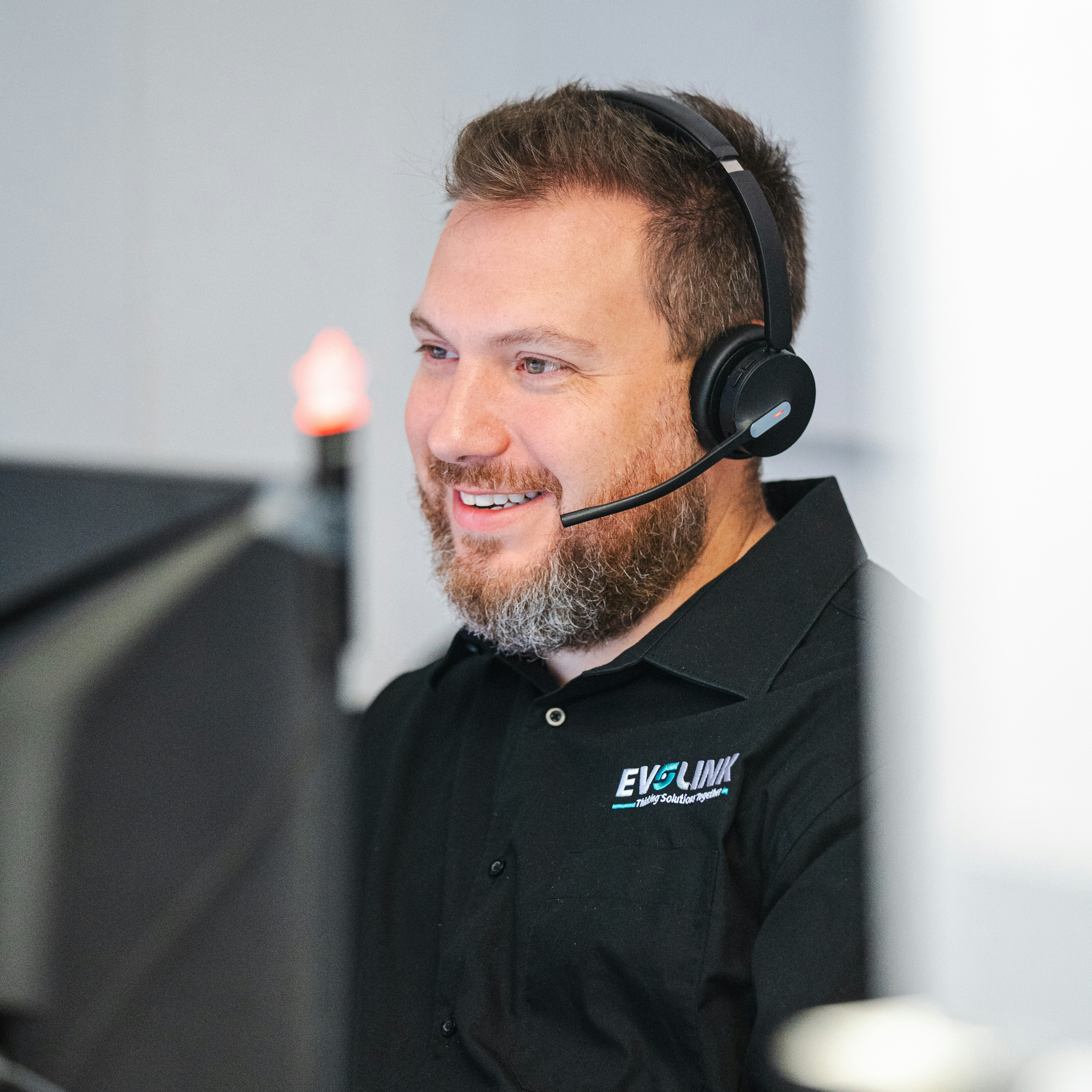 Un agent du service client d'Evolink, tout sourire, vêtu d'un t-shirt noir aux couleurs de l'entreprise, porte un casque d'écoute alors qu'il travaille à son bureau.