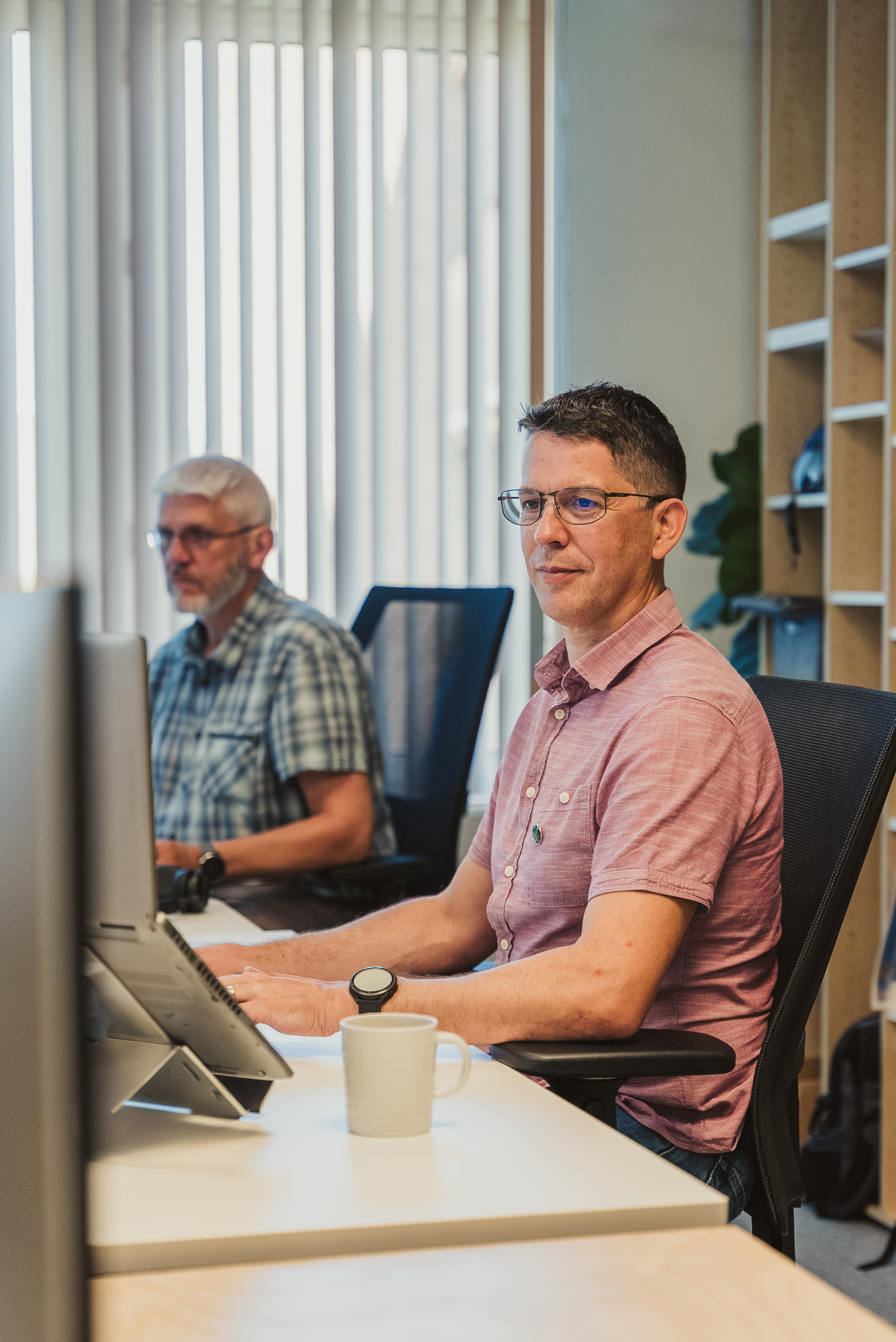 Two men work at desktop computers in a bright Ecopower office, one looking towards the camera.