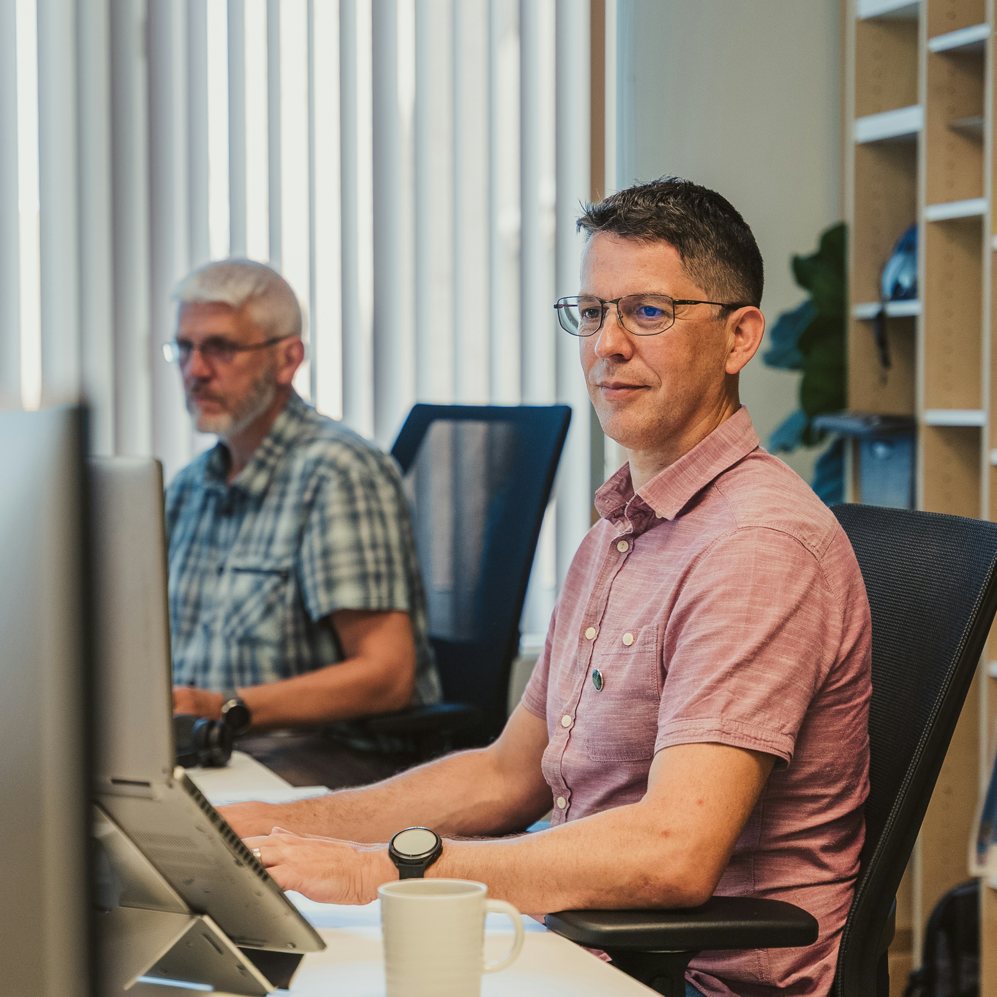 Two men work at desktop computers in a bright Ecopower office, one looking towards the camera.