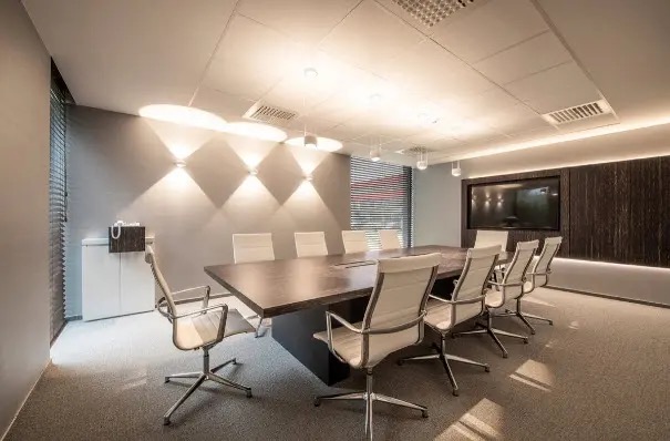 Modern boardroom with a long dark wood conference table surrounded by white leather high-back chairs under warm downlighting.